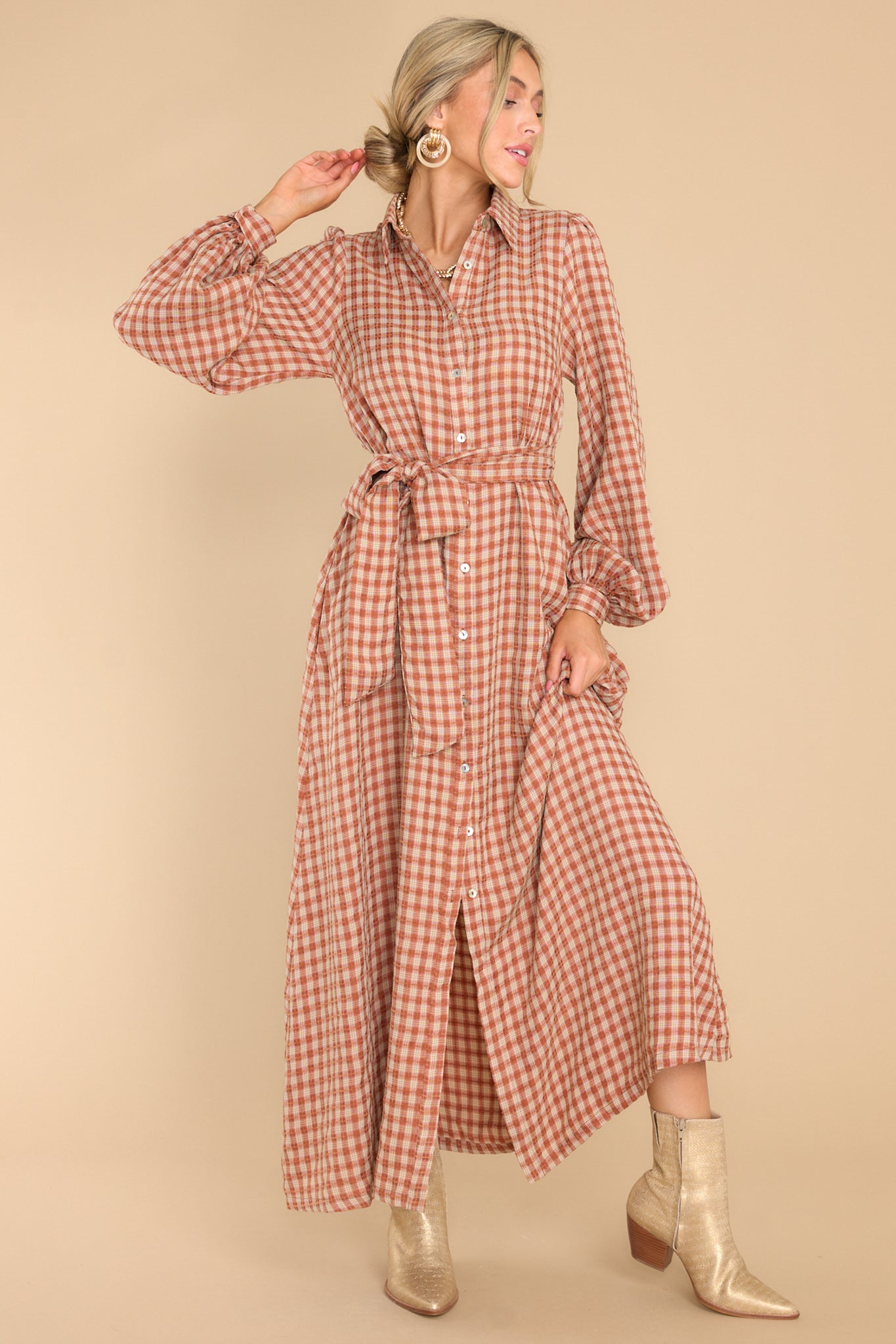 This brown dress features a collared neckline, functional buttons down the front, long sleeves with buttoned cuffs, two functional pockets, and adjustable self-tie belt.