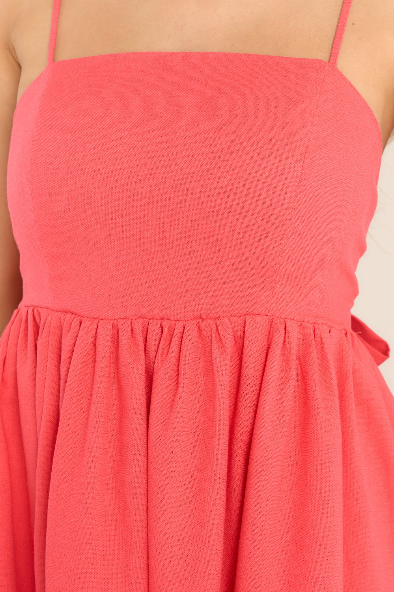 Close up view of this dress that features a square neckline, skinny adjustable shoulder straps, a back zipper with a wrap around self-tie bow, waist pockets, and flowy short skirt. 