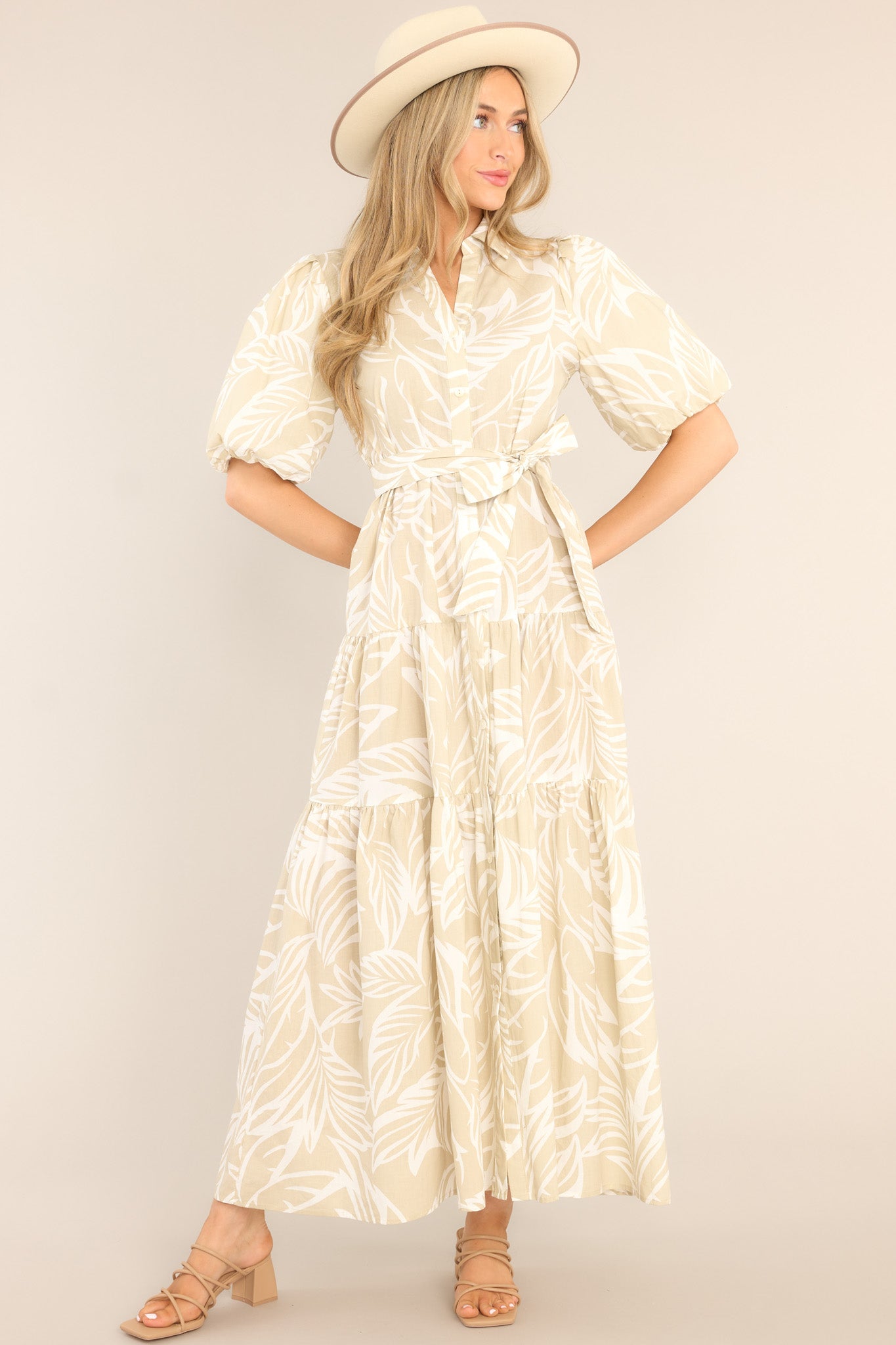 Front view of  this dress that features a collared neckline, functional buttons down the front, a self-tie belt, a tiered design, elastic cuffed sleeves, and a tropical palm frond print.