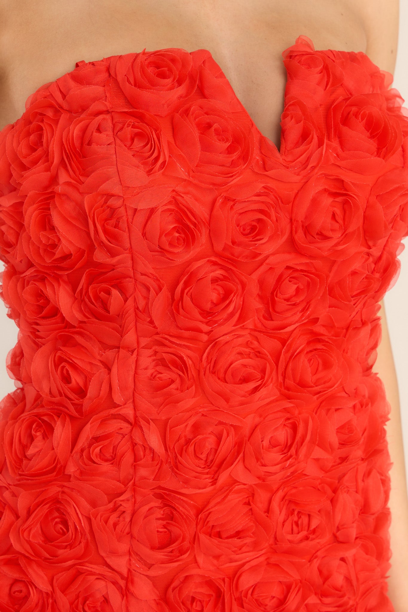 Close up view of this dress that features a strapless design with a v-cutout, a zipper and hook closure at the back of the bodice, and delicate, fabric roses throughout. 