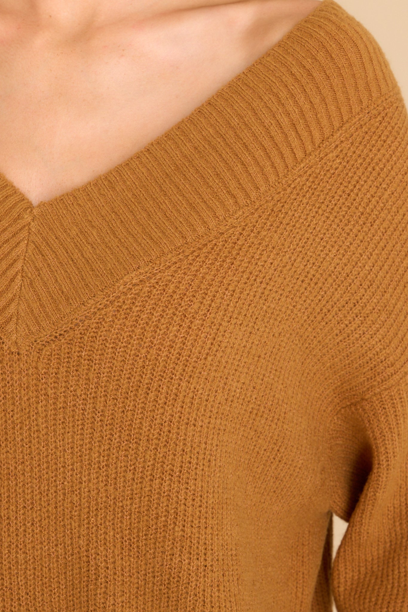 Close up view of this sweater that features a wide v-neckline, long sleeves with ribbed cuffs, a bottom hem that is longer in the back and has small slits up both sides, and a super soft feel throughout.