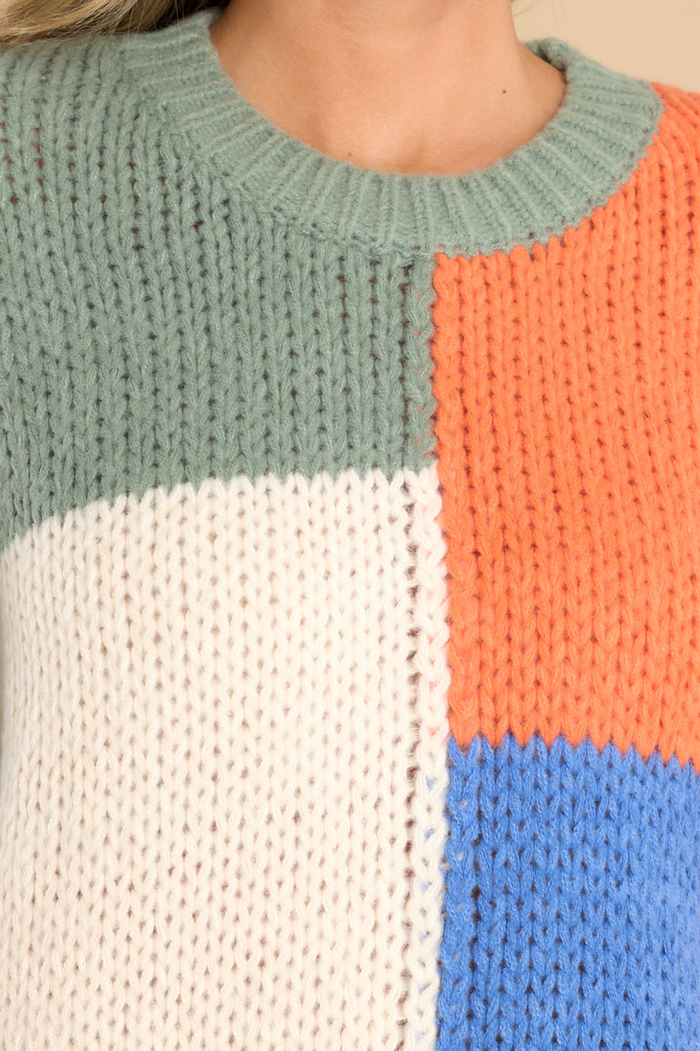 Close up view of this sweater that features a round neckline, long sleeves, a chunky knit design, and a colorblock pattern.