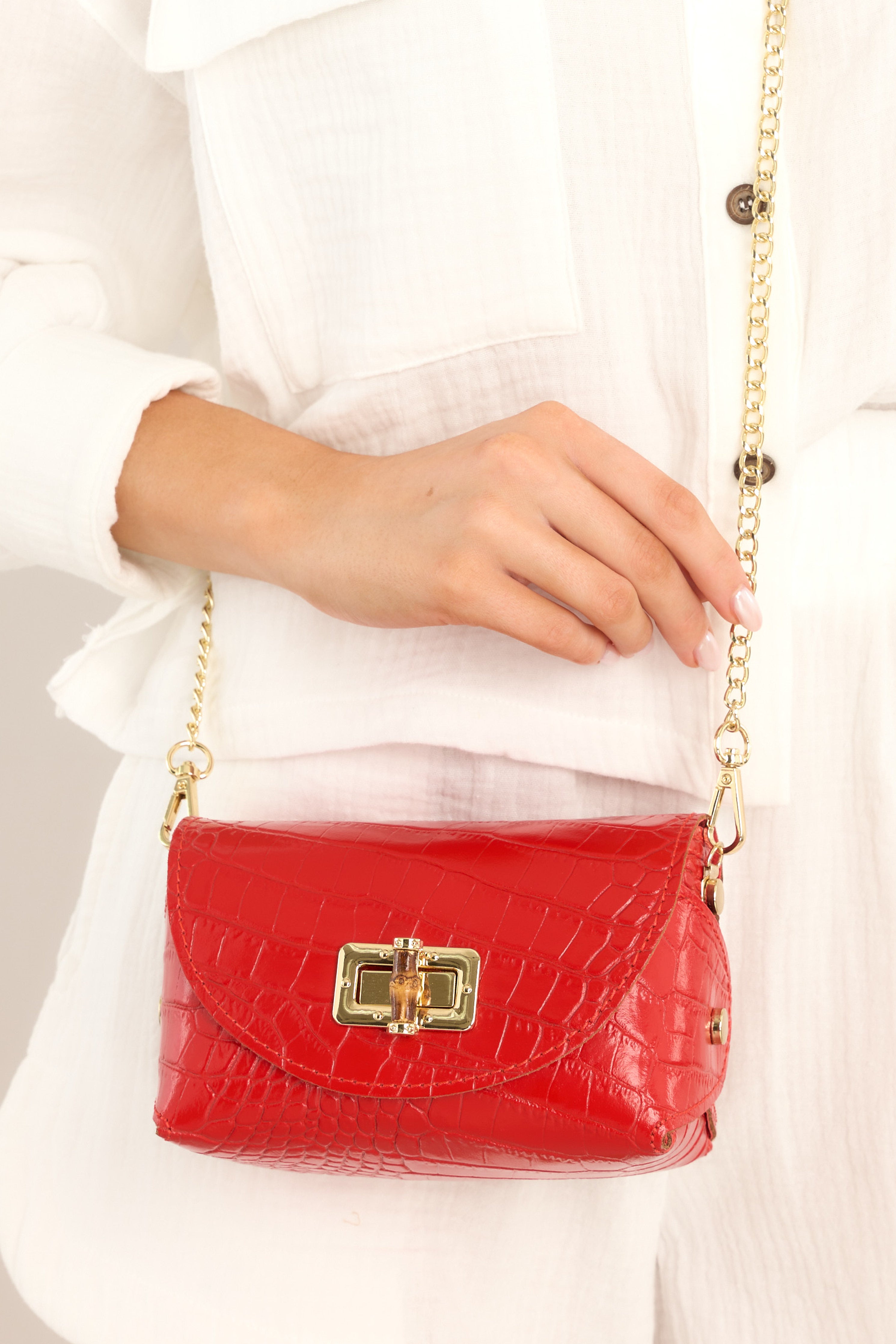Close up view of a red, vegan leather, textured handbag. This handbag features a gold clasp, as well as a gold strap. 