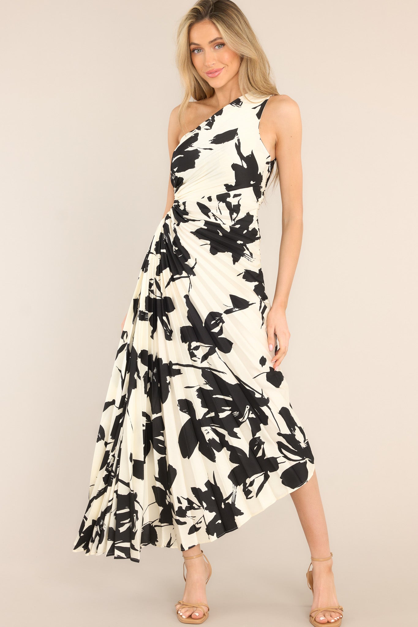 This black and ivory dress features an asymmetrical neckline, a side zipper, a circular waist cutout,  pleats throughout, and a high-low hemline.