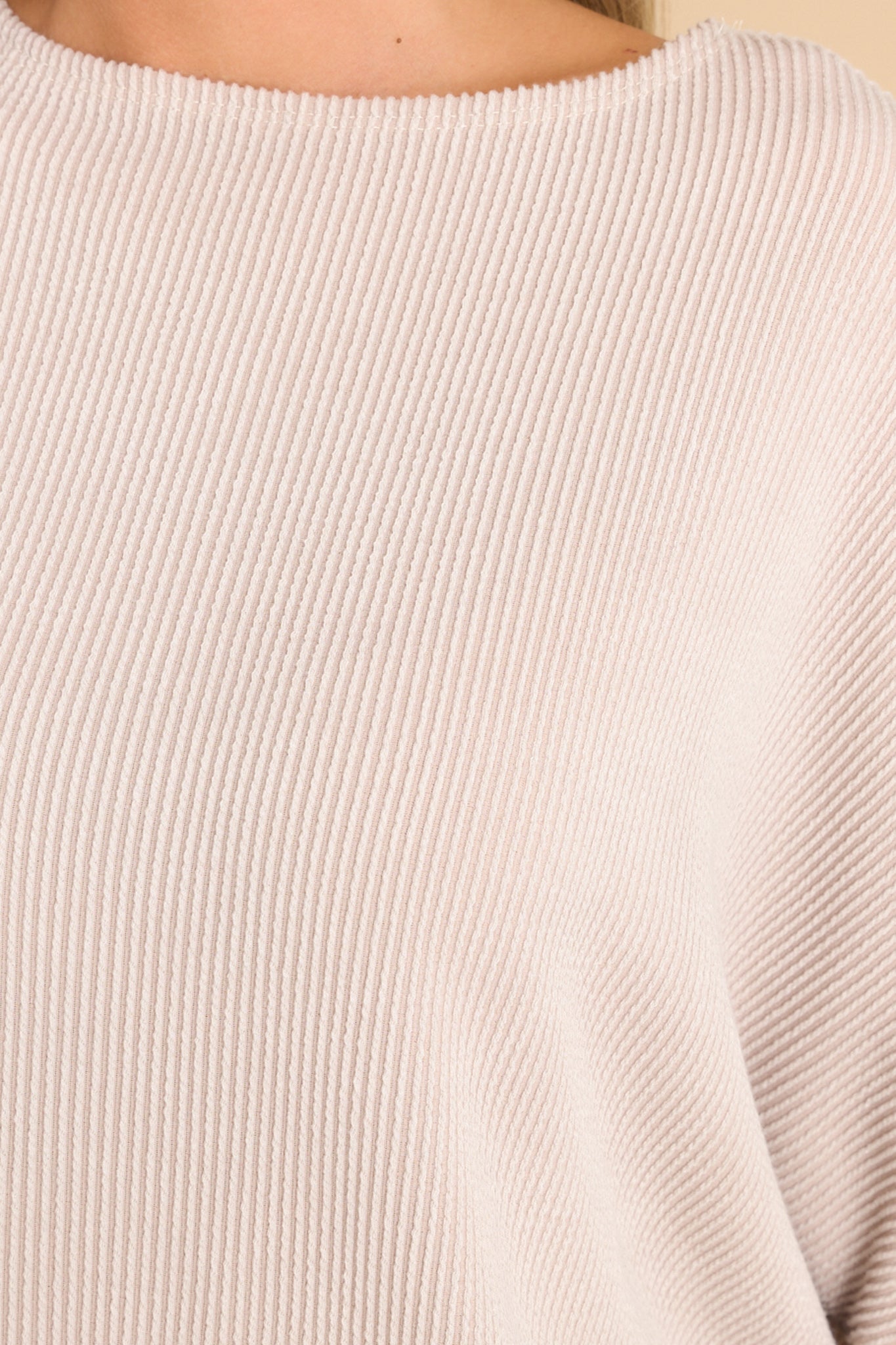 Close up view of this pullover top that features a round neckline, long dolman sleeves, and a slight high low hem line.