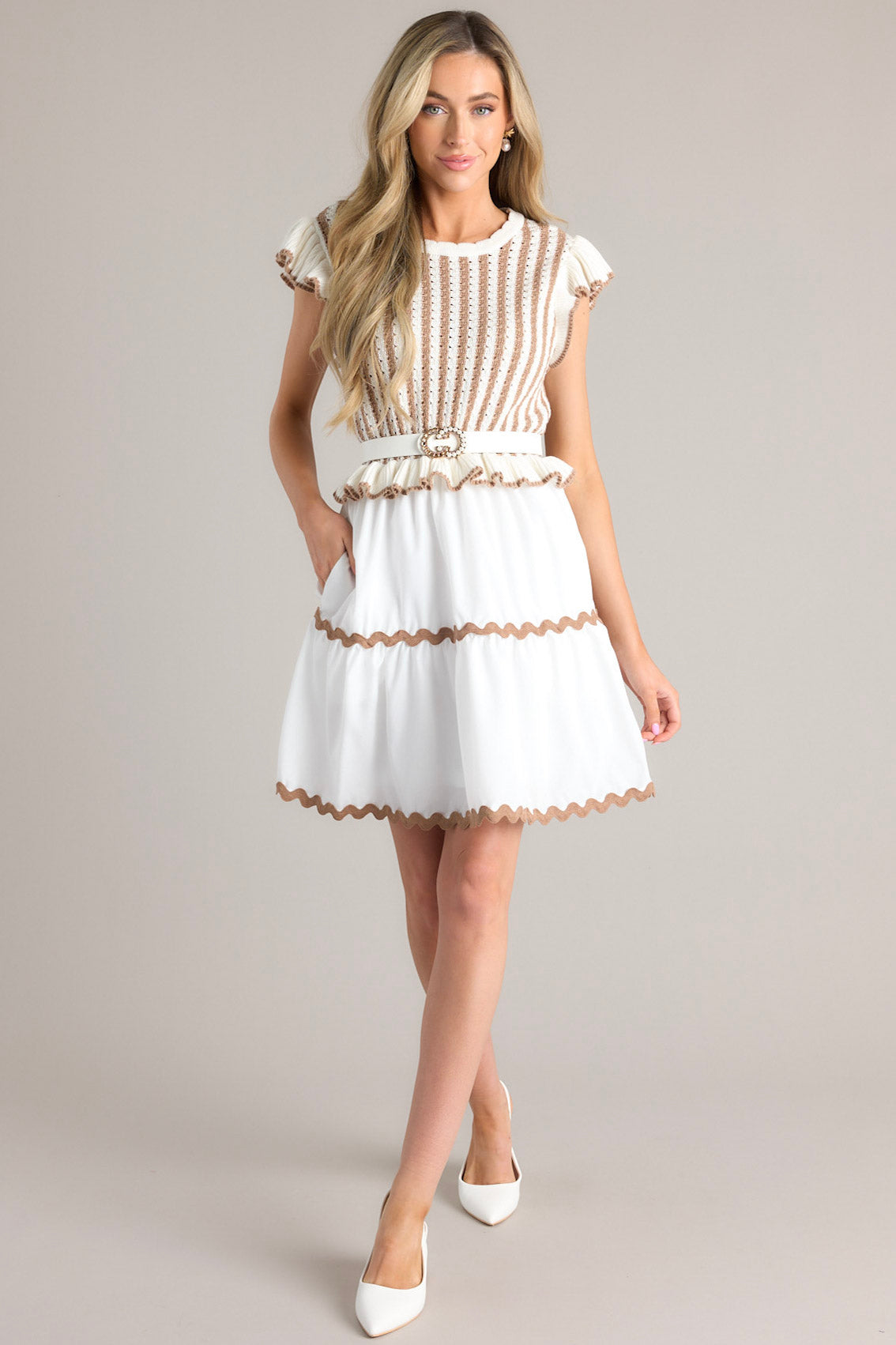 This white and brown dress features a scalloped crew neckline, a striped knitted bodice, a ruffled waistline, functional pockets, scalloped detailing, a scalloped hemline, and ruffled sleeves.