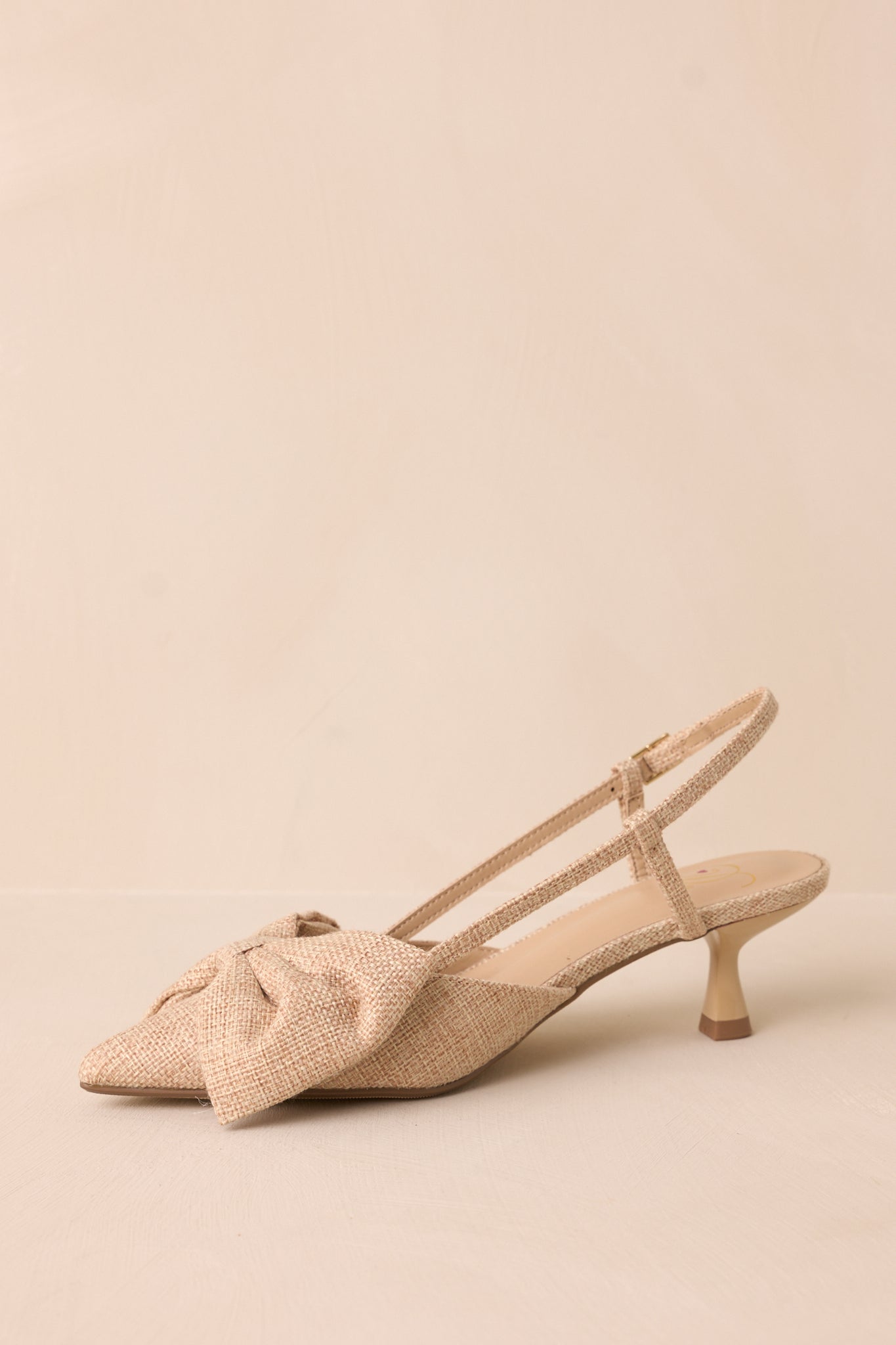 Another side shot highlighting the combination of the pointed toe, raffia bow, and the ankle strap's elegant placement.