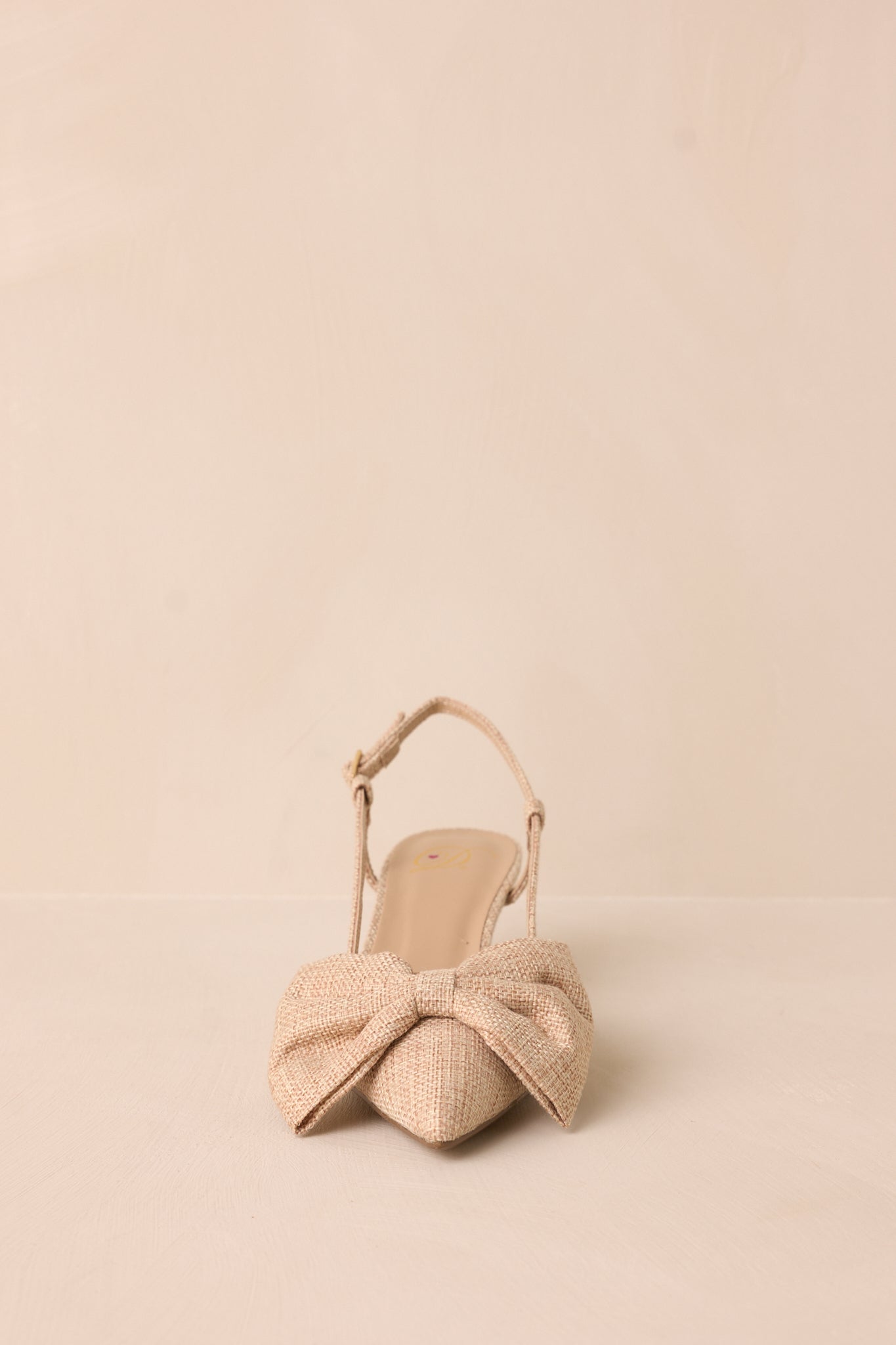 A close view of the raffia kitten heel, focusing on the pointed toe and the large raffia bow detail on the front.