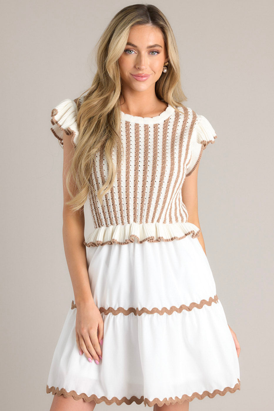 Full front view of this dress that features a scalloped crew neckline, a striped knitted bodice, a ruffled waistline, functional pockets, scalloped detailing, a scalloped hemline, and ruffled sleeves.