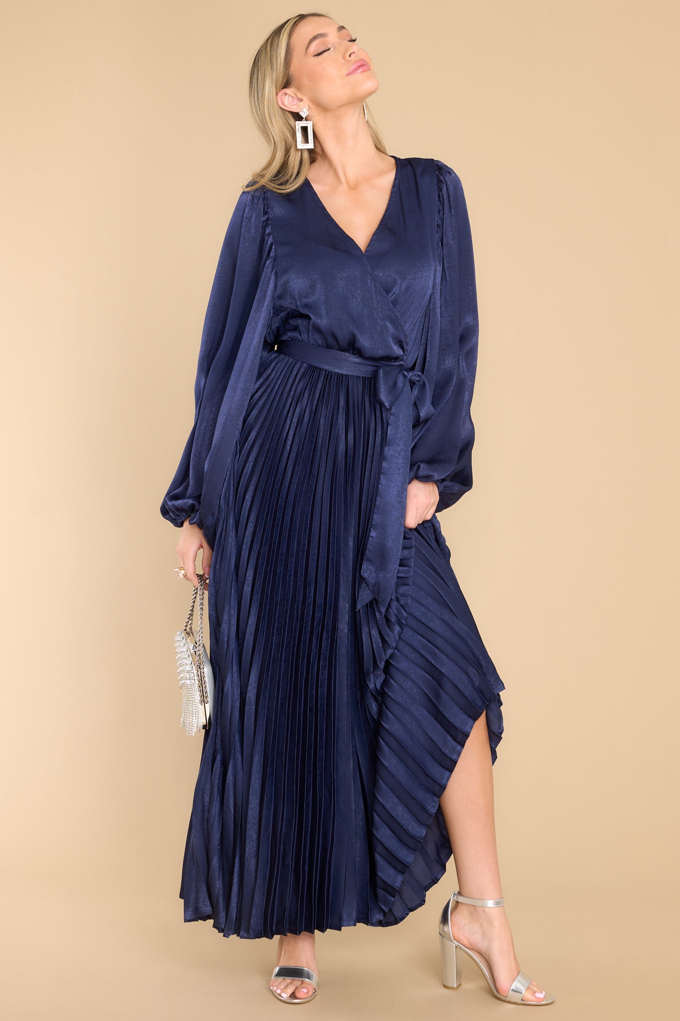 Front view of  this dress that features a v-neckline with a button clasp, flowy sleeves with elastic cuffs, an elastic waistband, a self-tie, and a pleated skirt. 