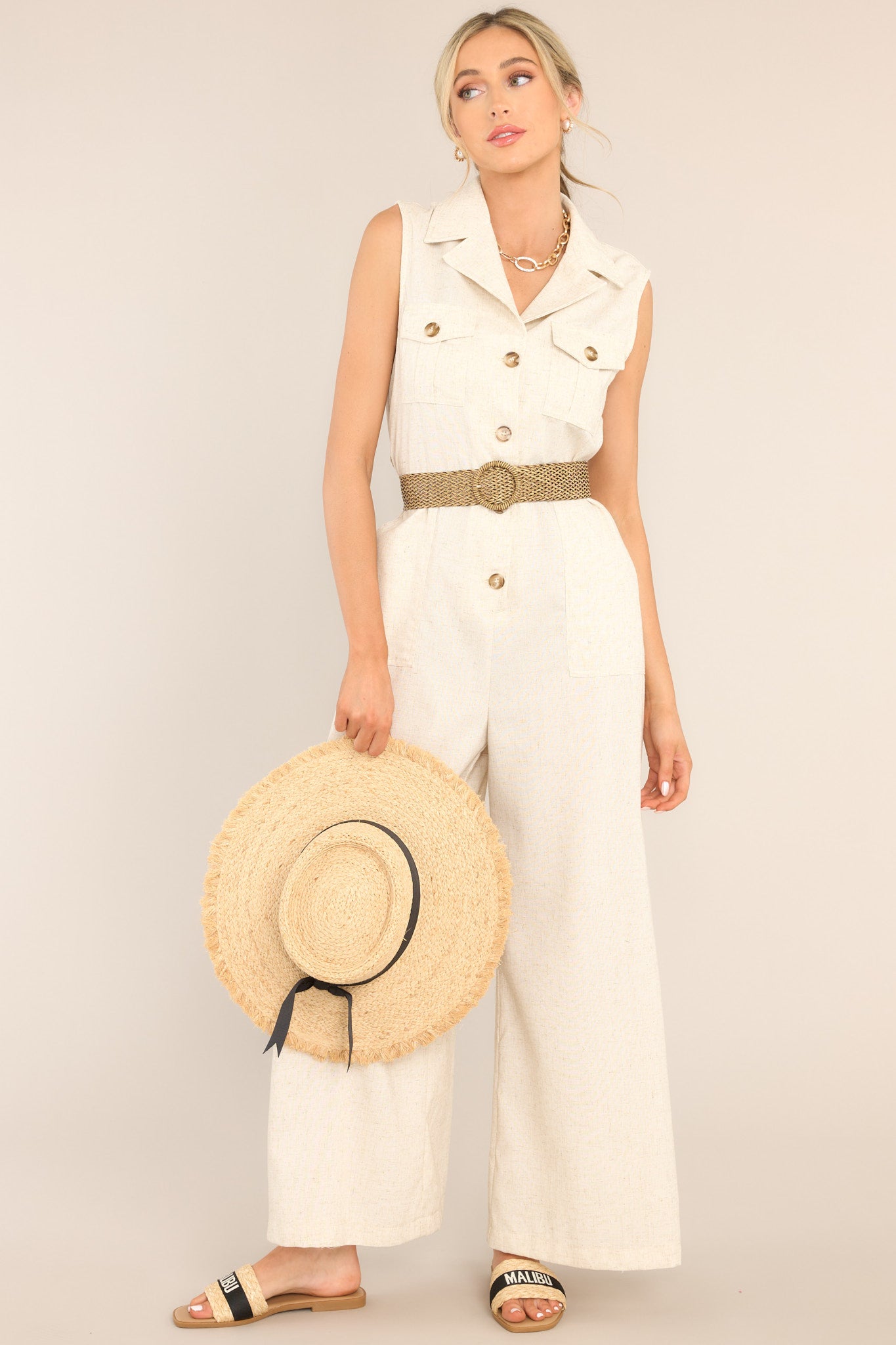 This jumpsuit features a notched lapel collared neckline, chest pockets, a functional button front, belt loops, an adjustable belt, an elastic insert at the back of the waist, hip pockets, and a wide leg.