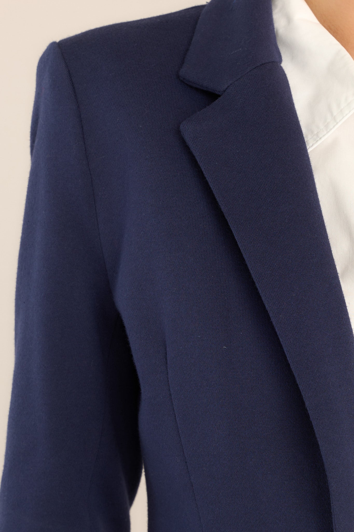 Close up view of this blazer that features a notch lapel collar, shoulder pads, a functional button, faux pockets, and faux buttons on the sleeves.