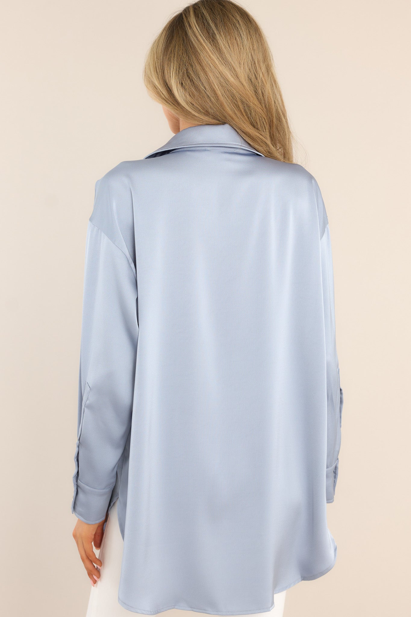 Back view of this top that features a collared neckline, functional gold buttons down the front, long sleeves with buttoned cuffs, a round hemline, and satin-like fabric.