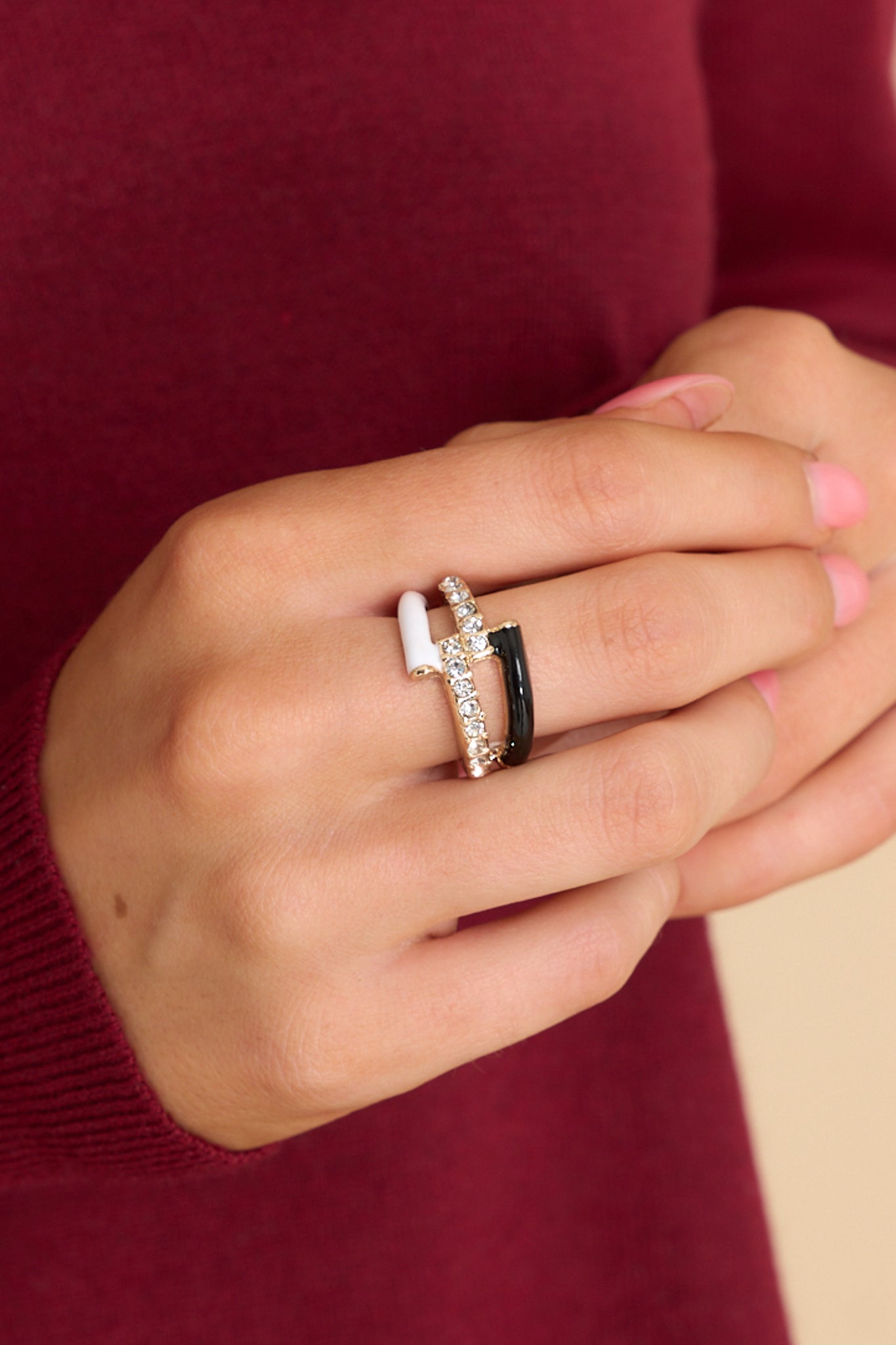 Styled shot of model wearing ring that features gold hardware, black and white accents, rhinestone detailing, and elastic under the band.