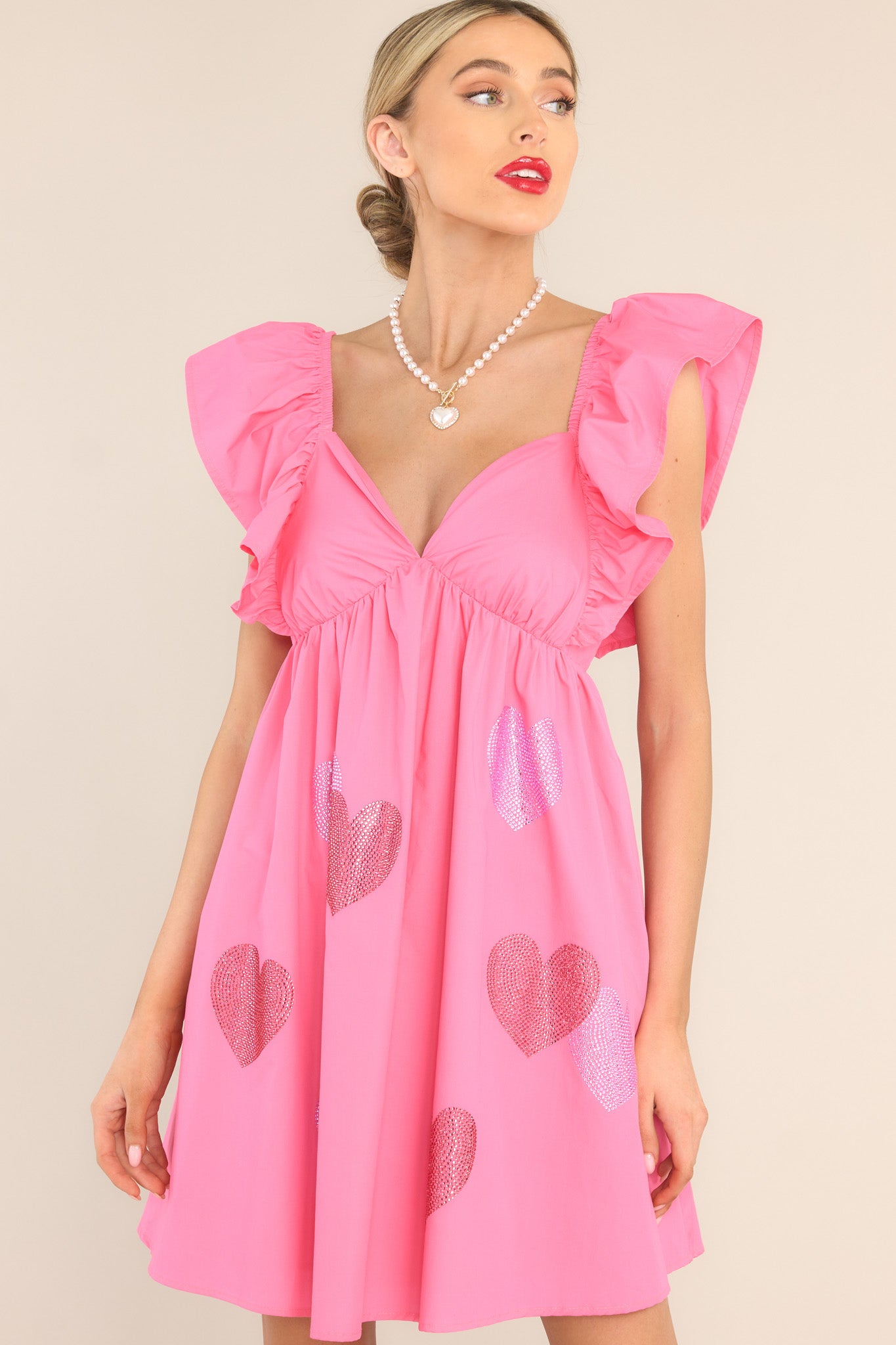 Front view of this dress that features a sweetheart neckline, flutter sleeves, rhinestone heart detailing, functional pockets, and a self-tie bow and zipper in the back. 