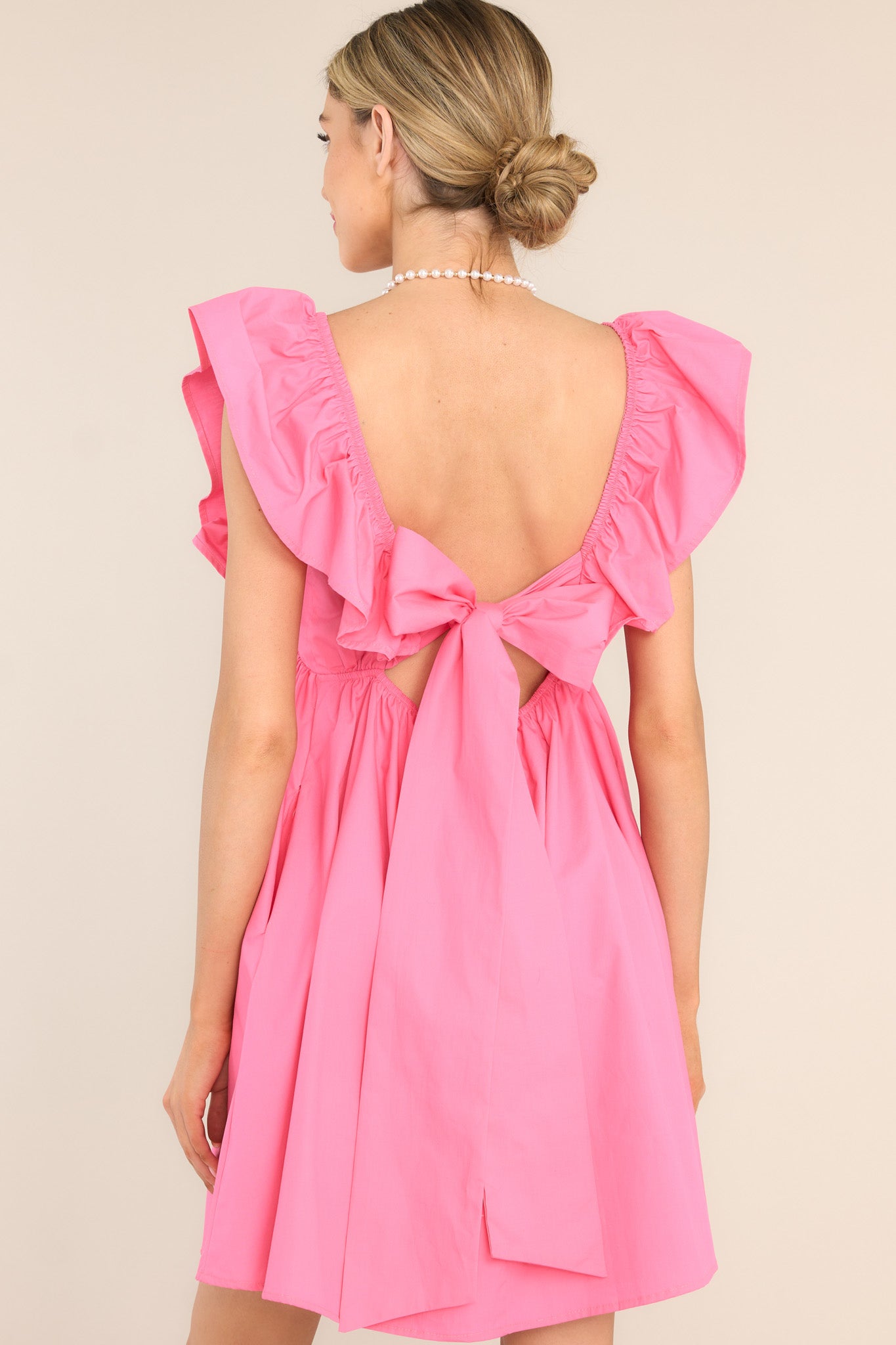 Back view of this dress that features a sweetheart neckline, flutter sleeves, rhinestone heart detailing, functional pockets, and a self-tie bow and zipper in the back. 