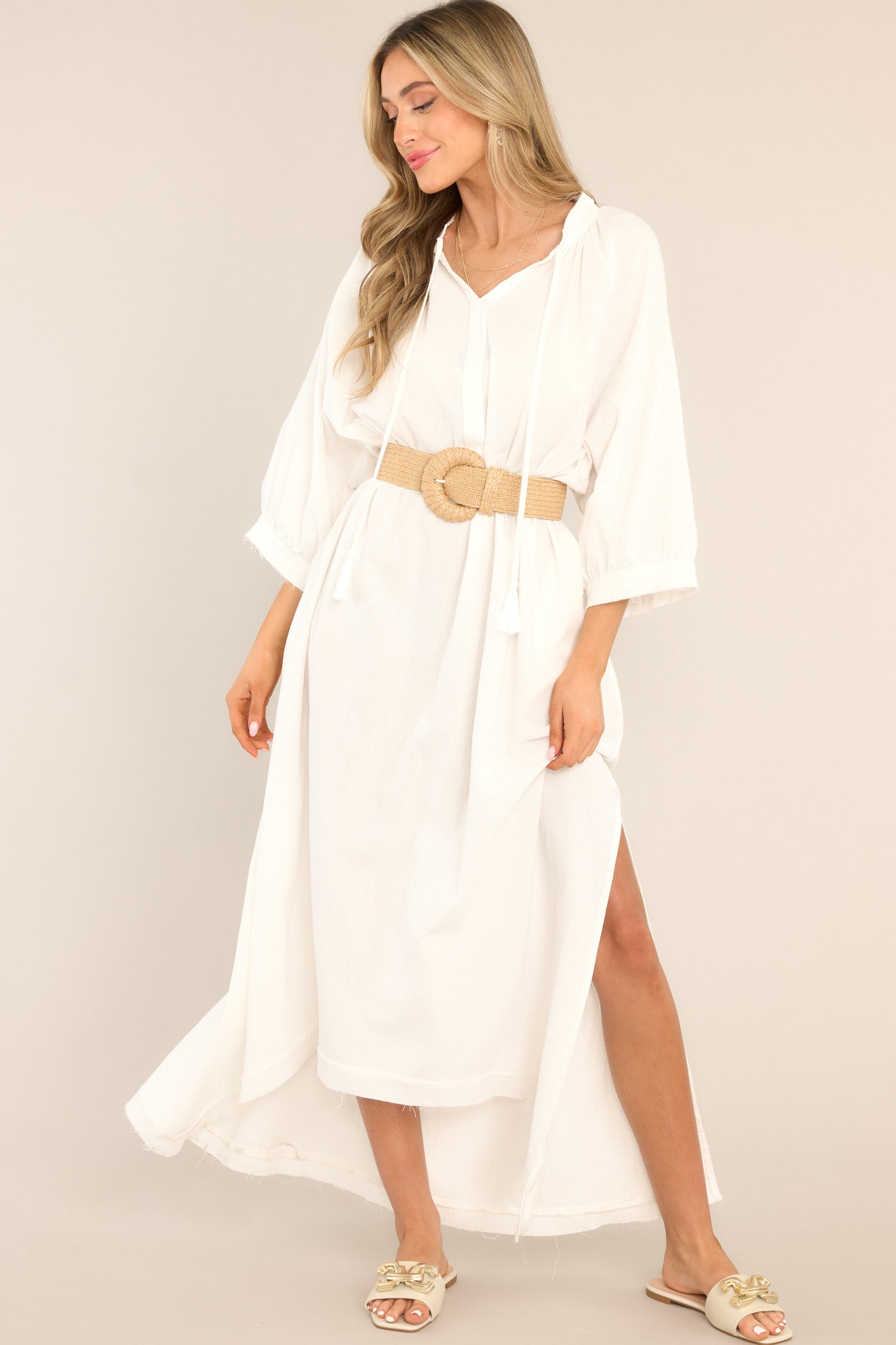 This ivory dress that features a tassel tie neckline, a front slit, functional waist pockets, and lightweight cotton fabric.