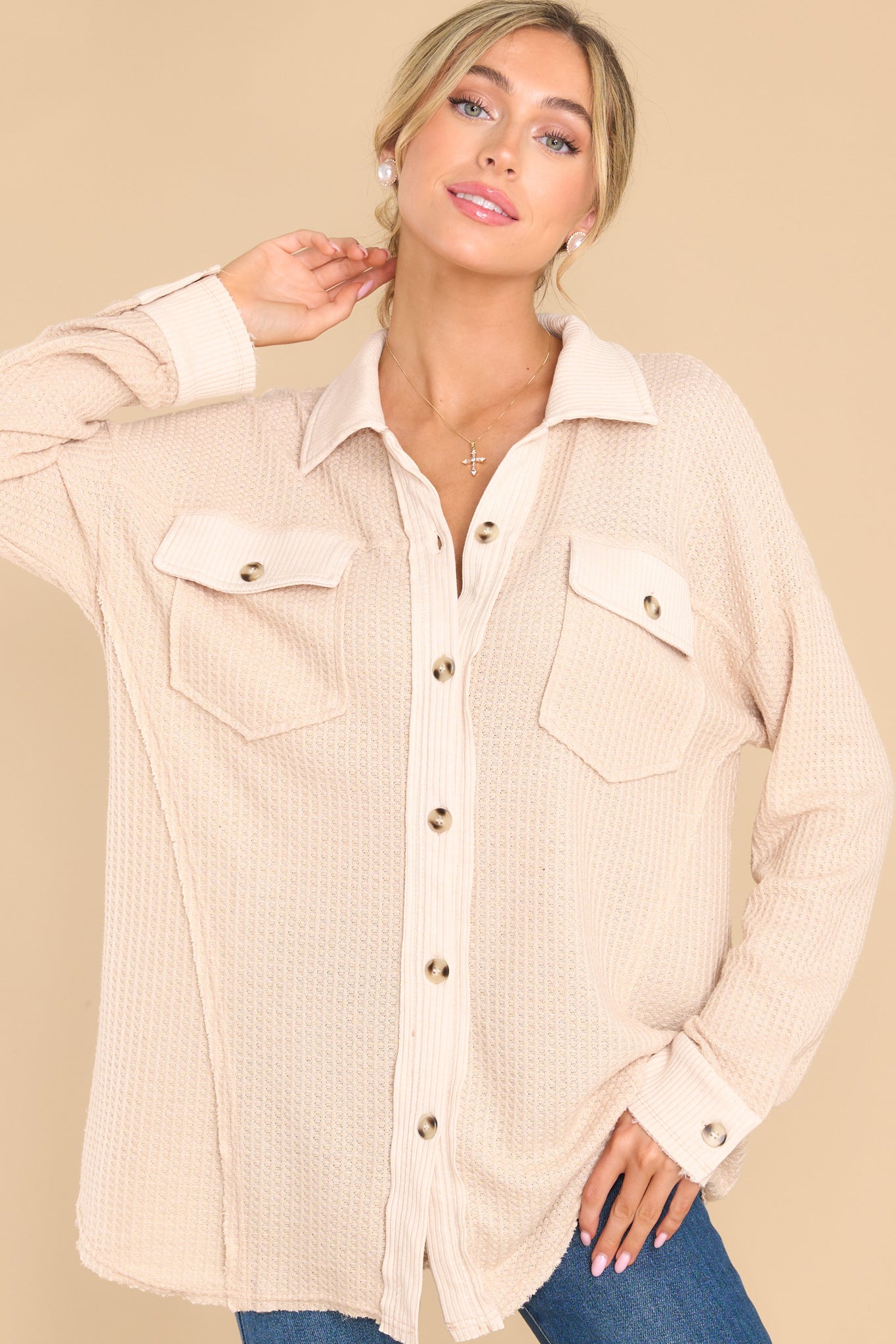 This tan top features a collared neckline, functional buttons down the front, bust pockets with button closures, long sleeves with buttoned cuffs, and a mixed-textured design throughout.