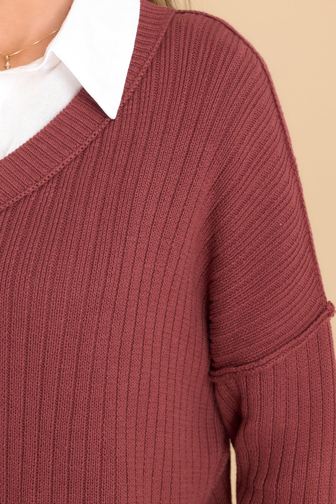 Close up view of this sweater that features a v-neckline, long sleeves with tapered cuffs, small slits up the bottom hem on both sides, and a knit texture throughout.