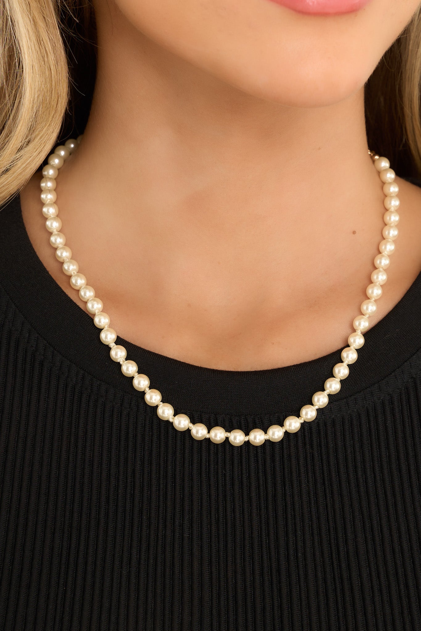 Detail shot of this pearl necklace that features gold hardware, a string of faux pearls, and a lobster claw closure.