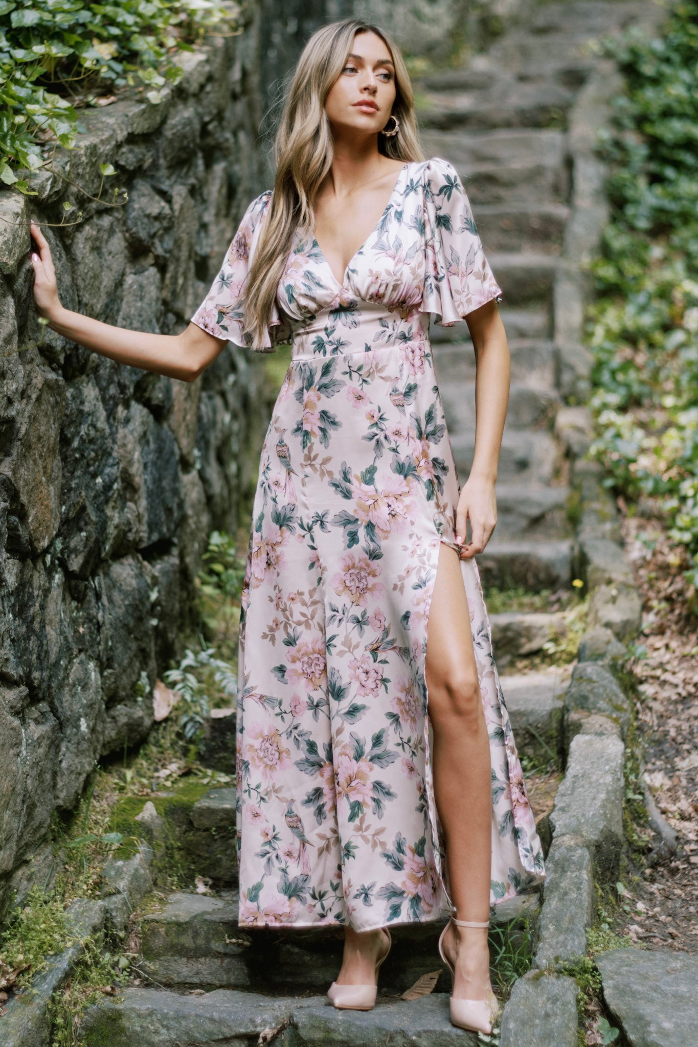 This maxi dress features a deep V-neckline, flutter sleeves, a fitted waist, A-line skirt, and a floral print with a subtle front slit.