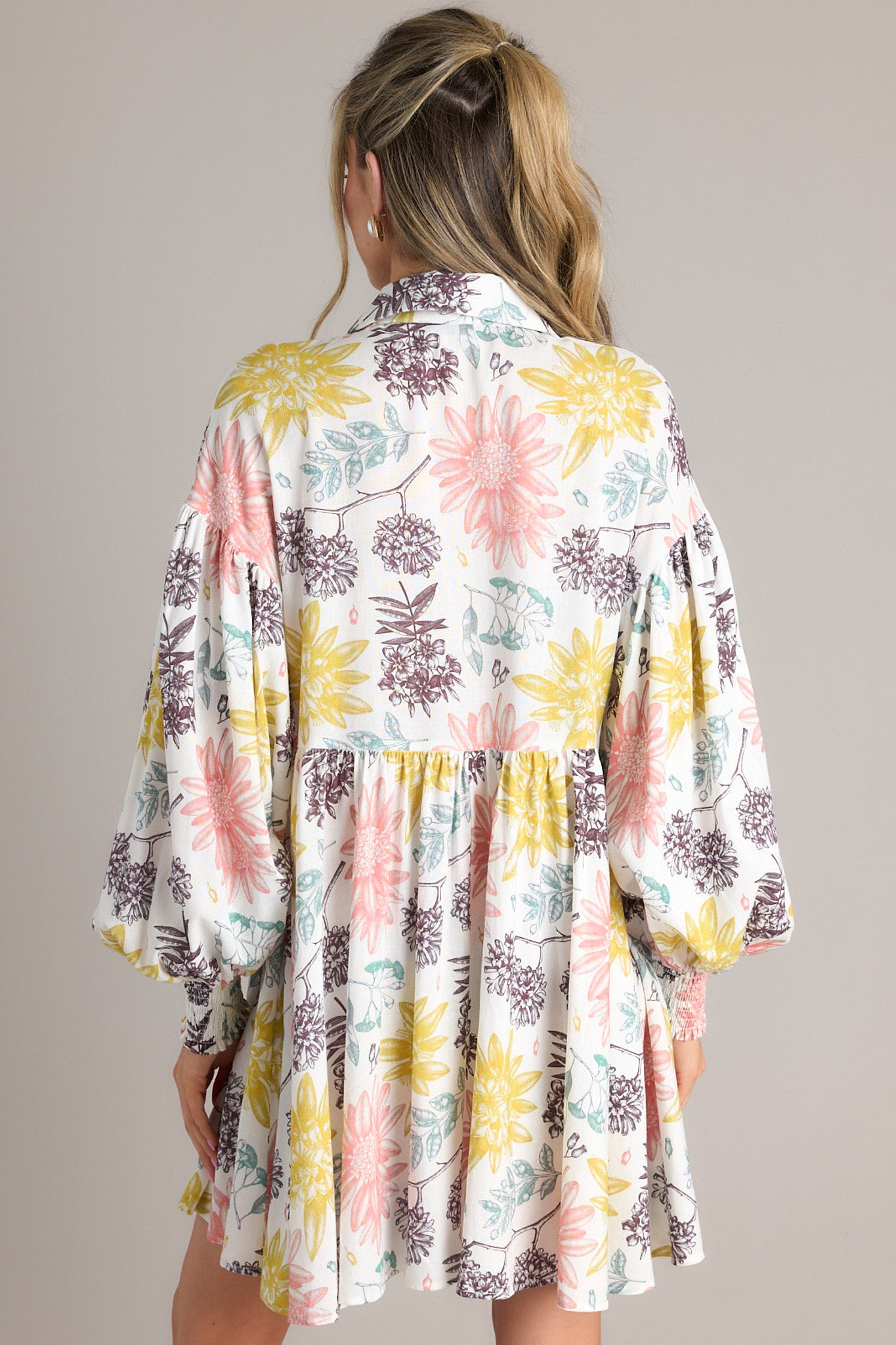 Back view of this dress that features a collared neckline, functional buttons down the front, long balloon sleeves with smocked cuffs, and a flowy, relaxed fit throughout.