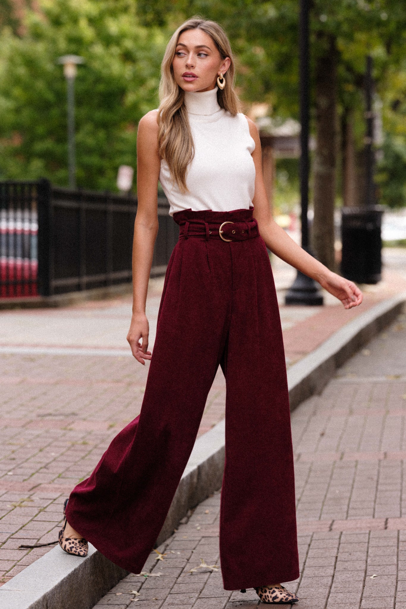 Full length view of burgundy pants featuring a paper bag style waistline, an adjustable belt, a zipper closure, and very flowy legs