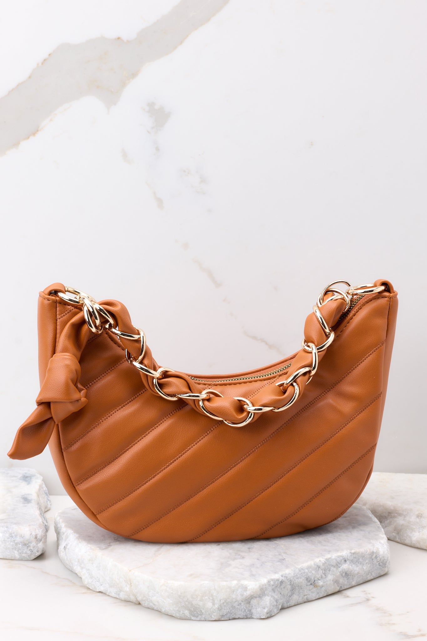 Front view of this bag that features a crescent-shaped design, a strap with an intertwined gold chain and faux leather detail, a zipper closure, a detachable round coin pouch, a detachable crossbody strap, and two pockets inside.