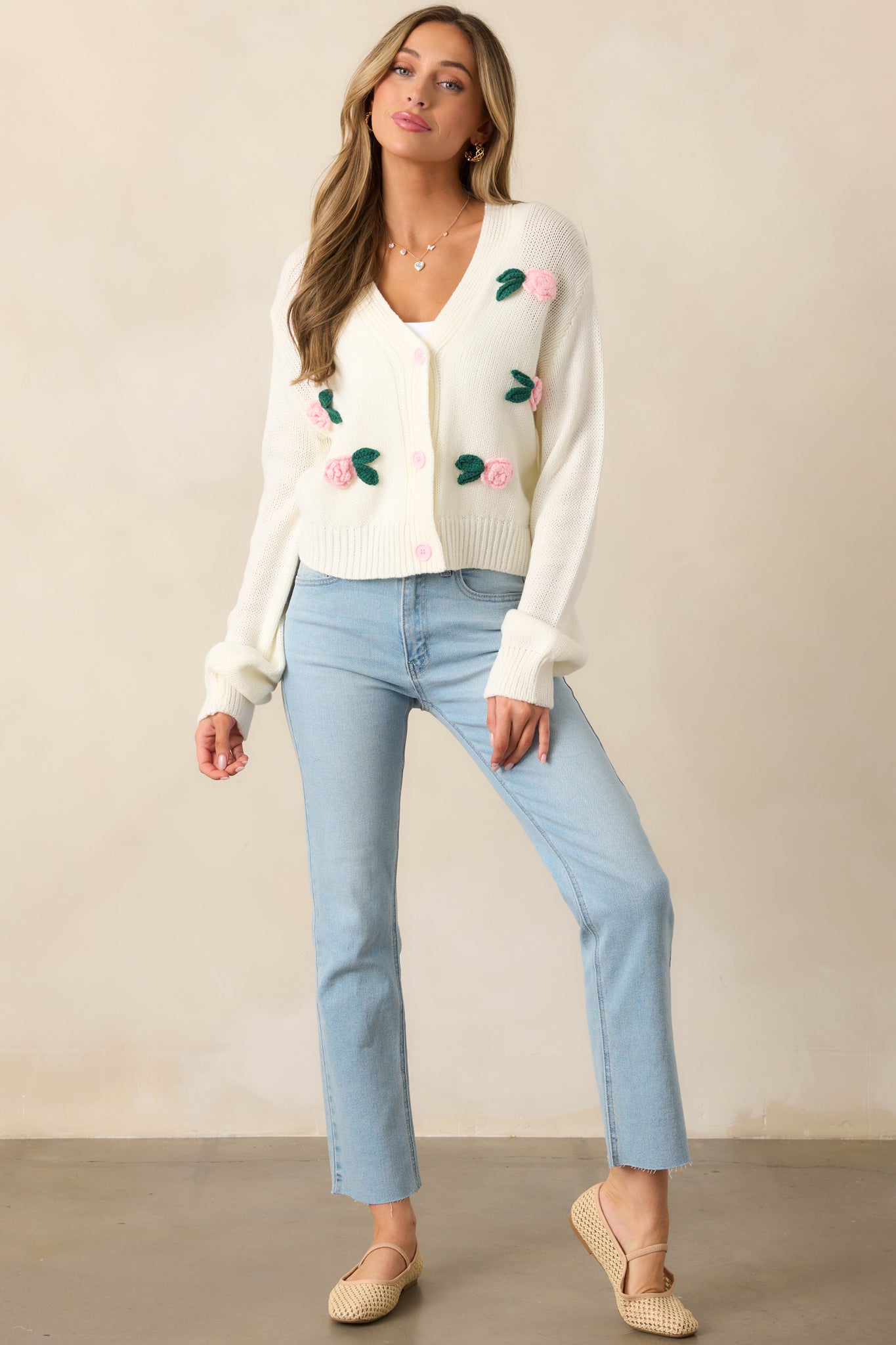 A delicate ivory cardigan with a V-neckline, light pink button front, and crochet rose appliques for a romantic touch.