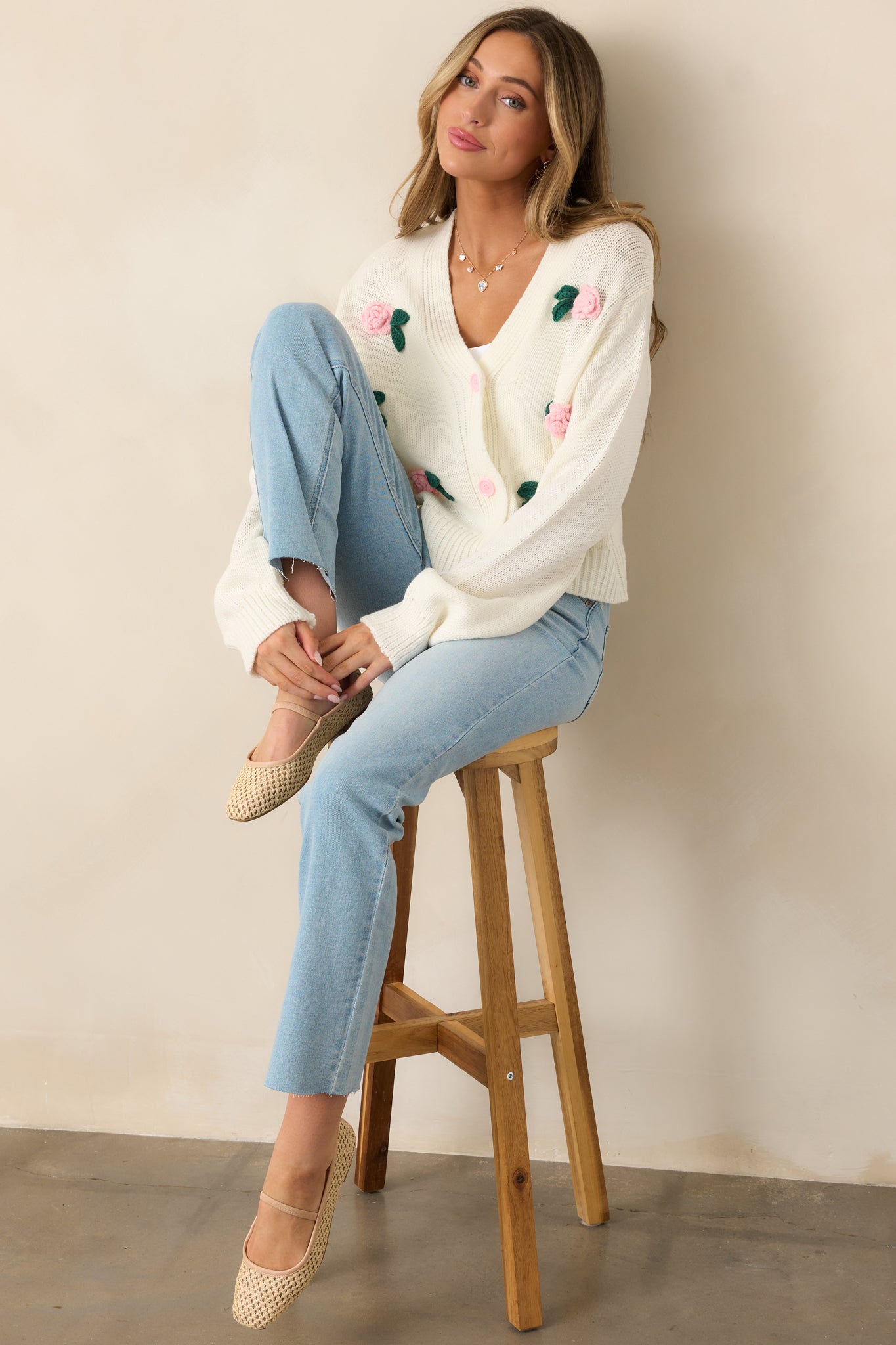 Soft and feminine, this ivory cardigan features long cuffed sleeves, a cozy knit texture, and floral appliques.