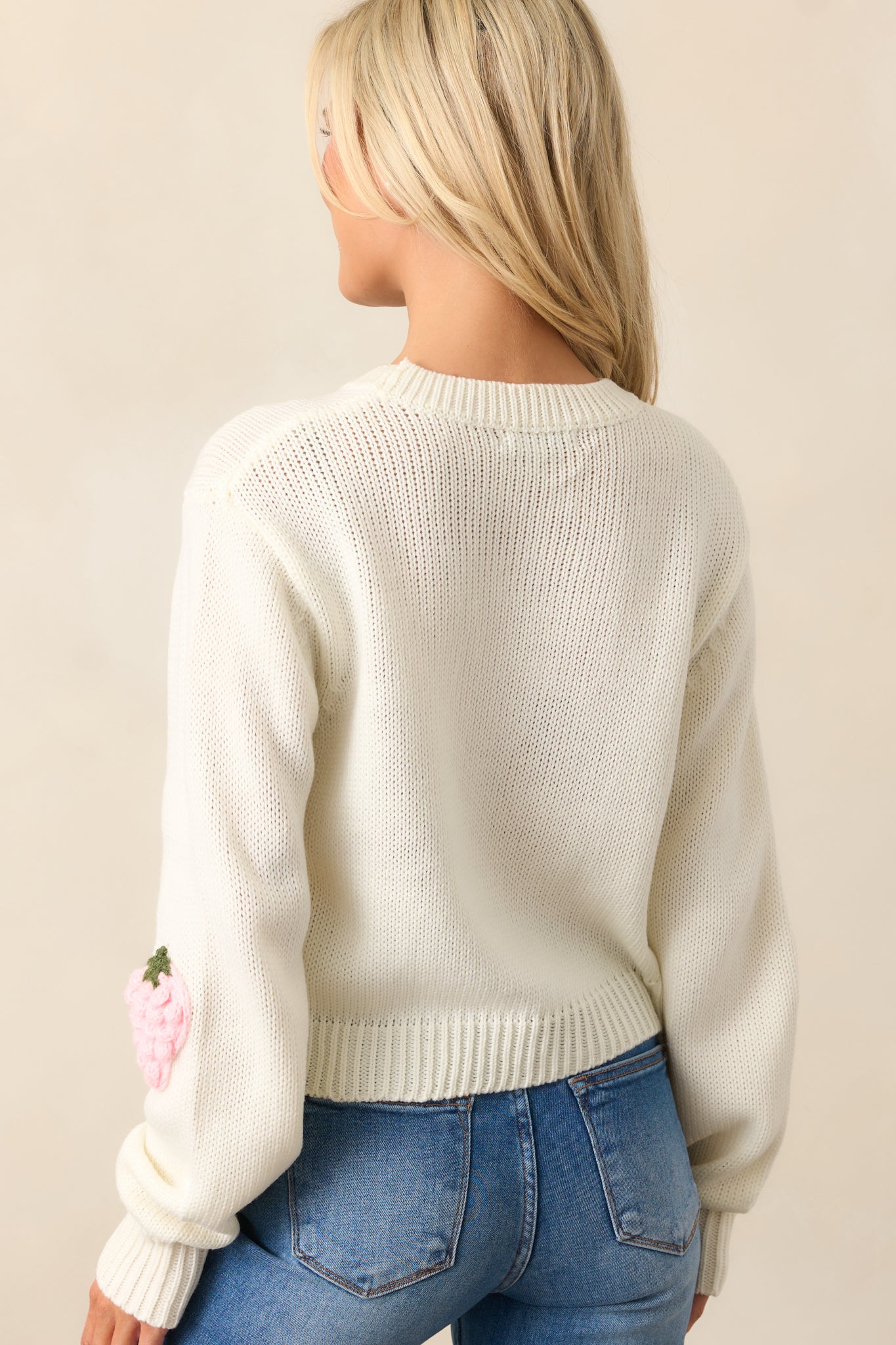 This ivory sweater features a round neckline, a slightly cropped length, relaxed fit, crochet strawberry appliques, and long sleeves with ribbed cuffs.