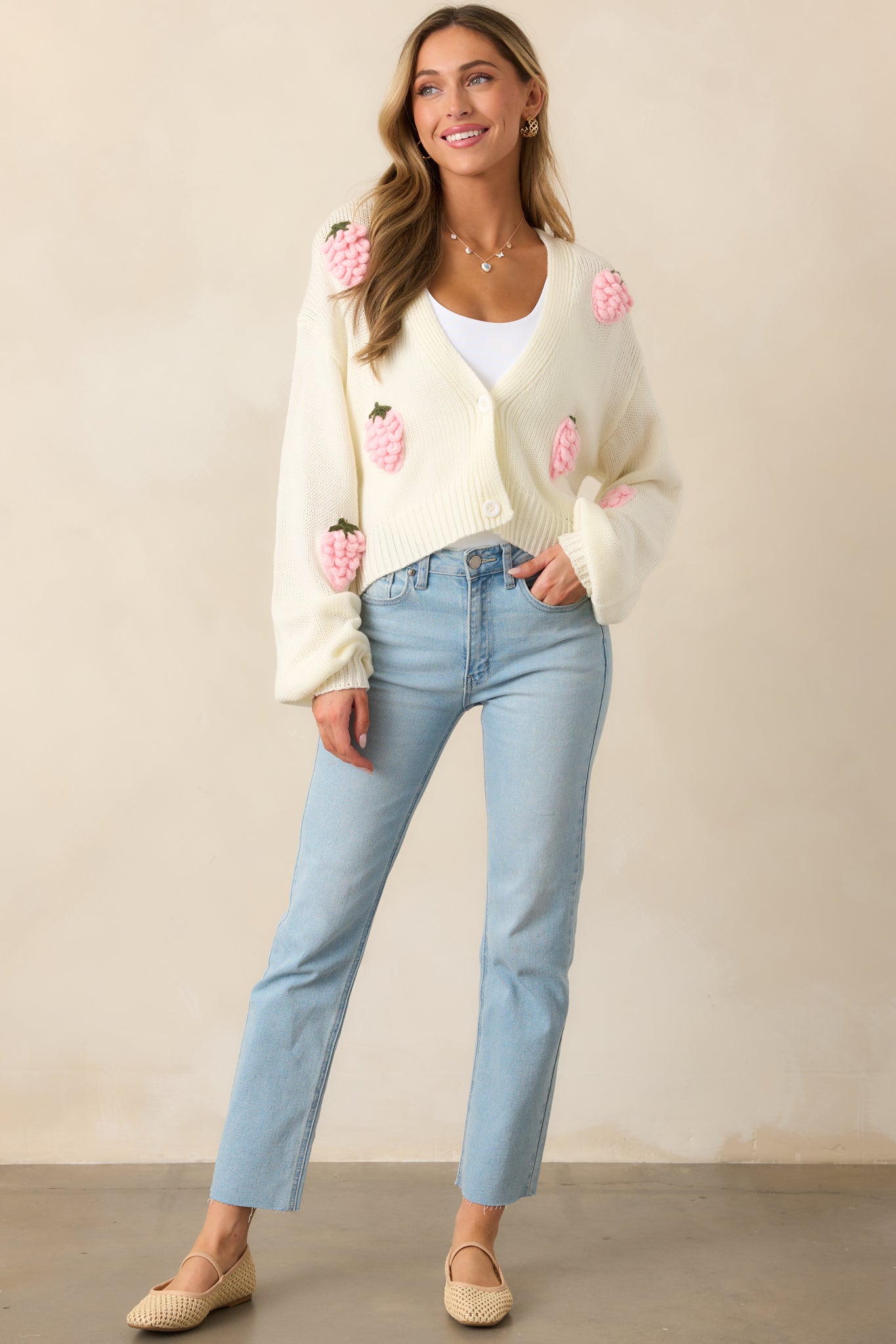 A charming ivory cardigan with a V-neckline, white button front, and playful crochet strawberry appliques