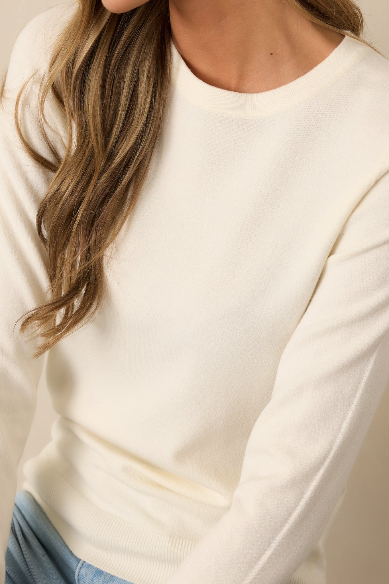 A zoomed-in view of the finely ribbed neckline and soft knit fabric of this ivory sweater.