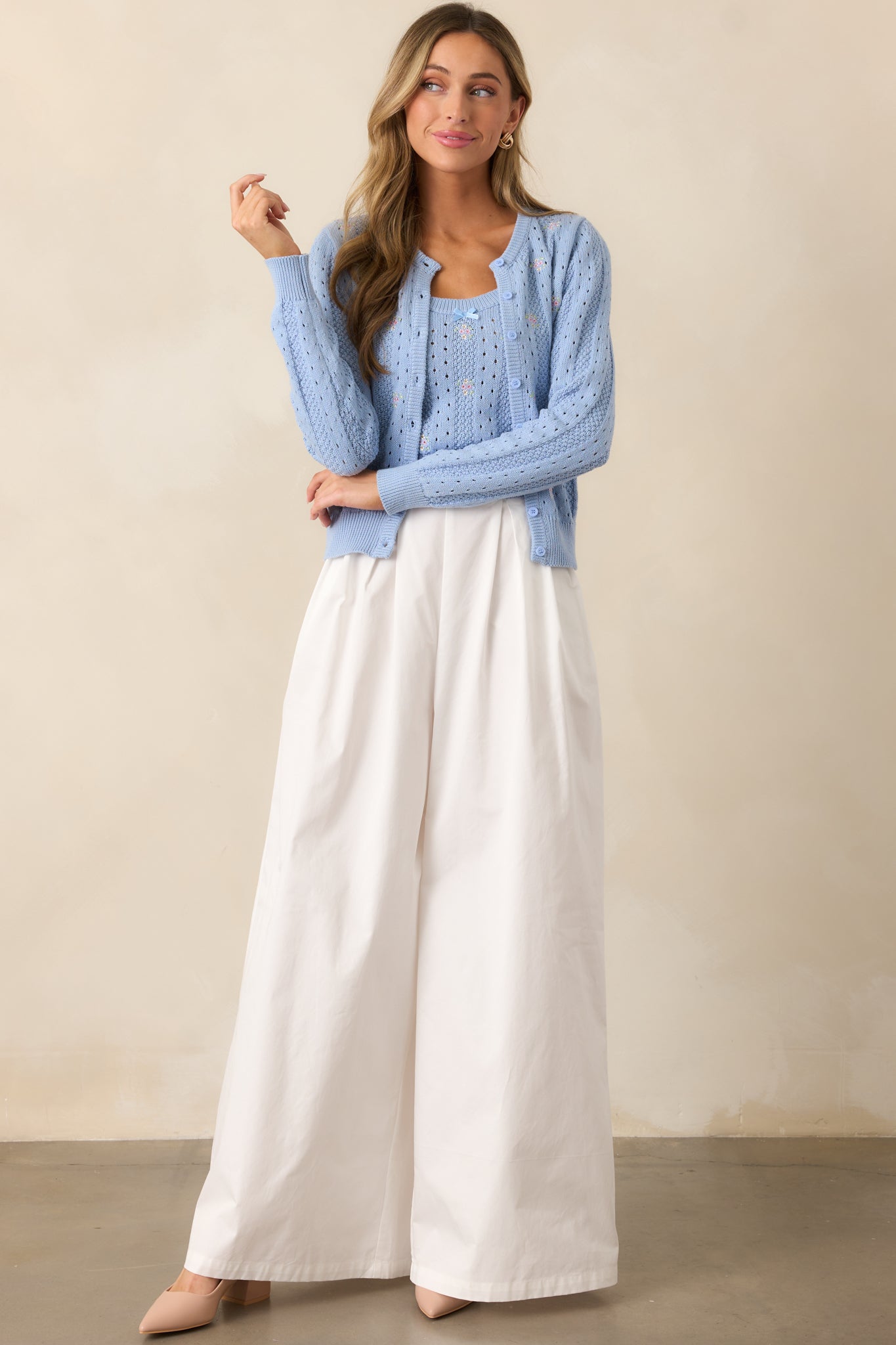 A blue cardigan with a rounded neckline, button front design, and long sleeves, displayed in full view to highlight its open knit pattern and floral embroidered details.