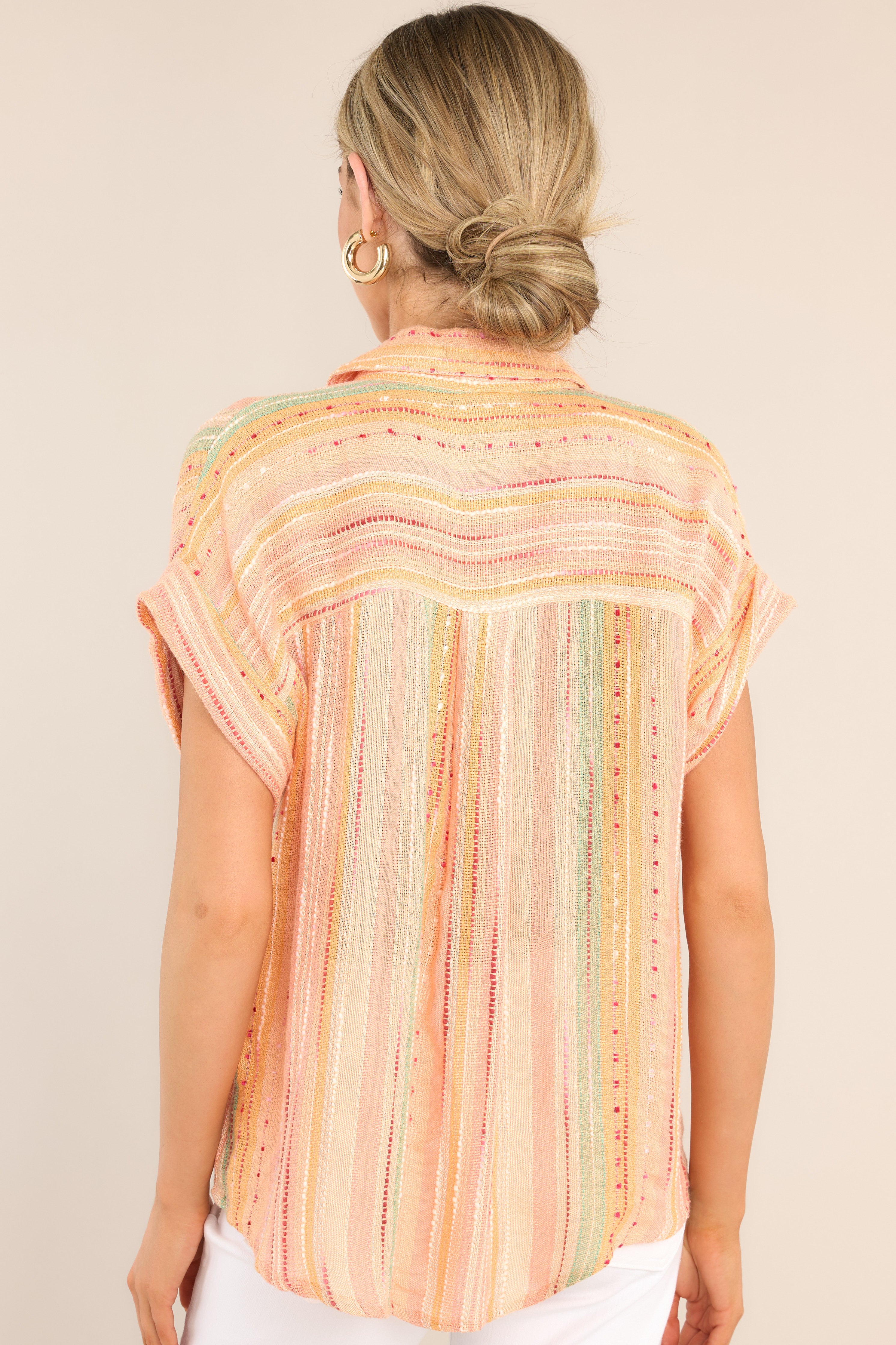 Back view of this top that features a collared neckline, functional buttons down the front, short sleeves with folded cuffs, a functional front pocket, and a round hemline.