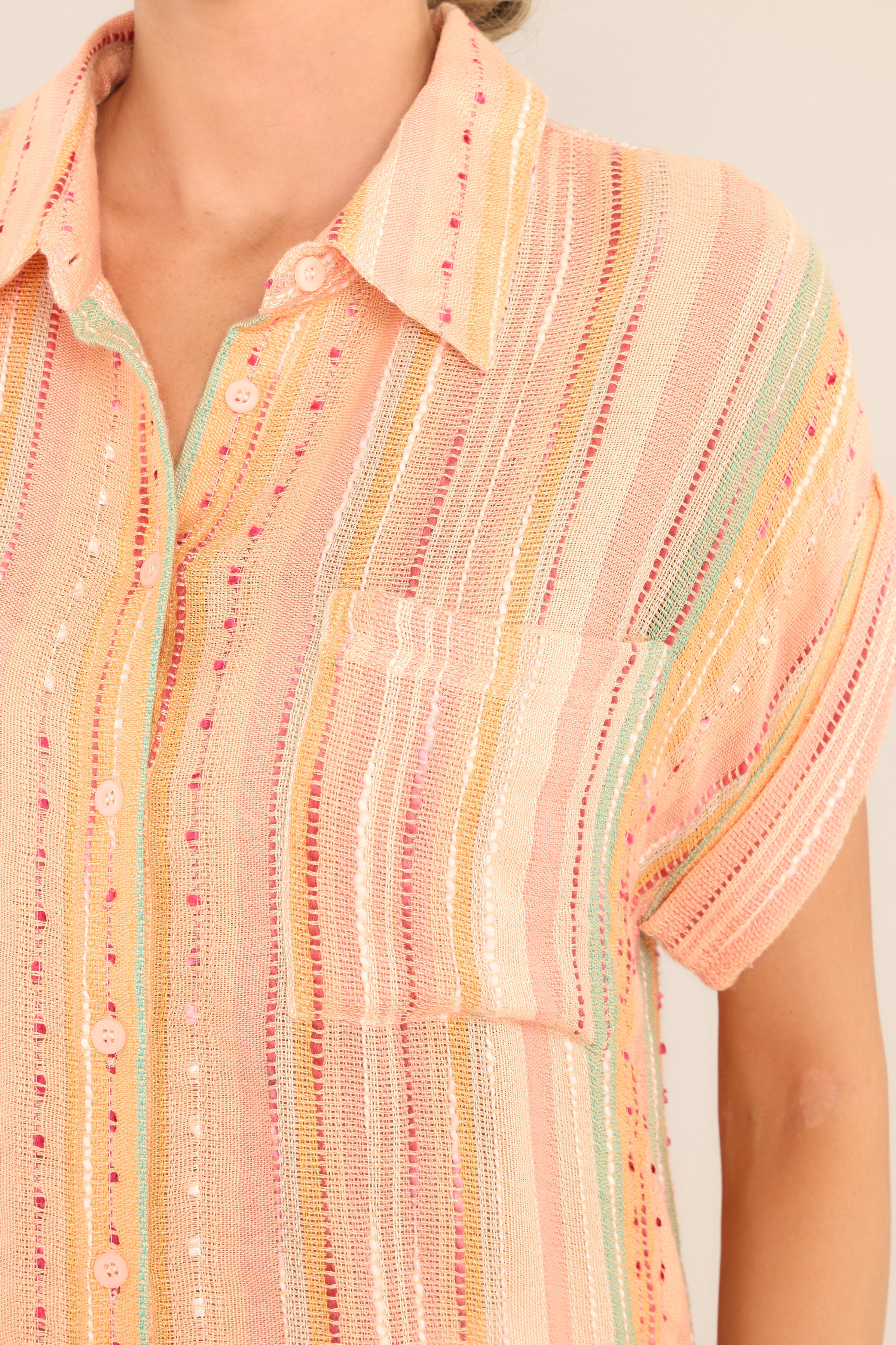 Close up view of this top that features a collared neckline, functional buttons down the front, short sleeves with folded cuffs, a functional front pocket, and a round hemline.