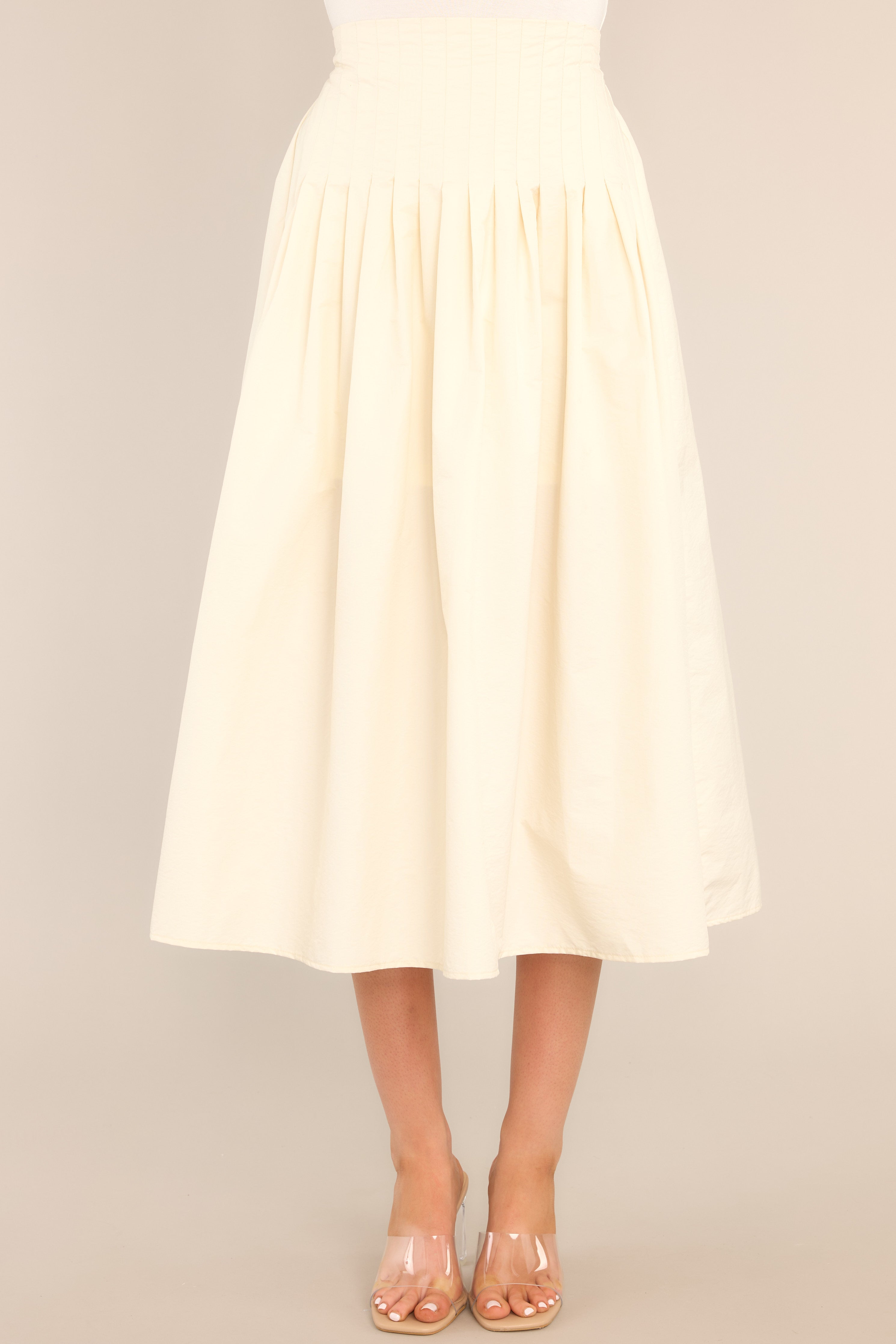 Full front view of this skirt that features a high waisted design, an elastic insert at the back of the waist, and intricate pleats around the hipline.