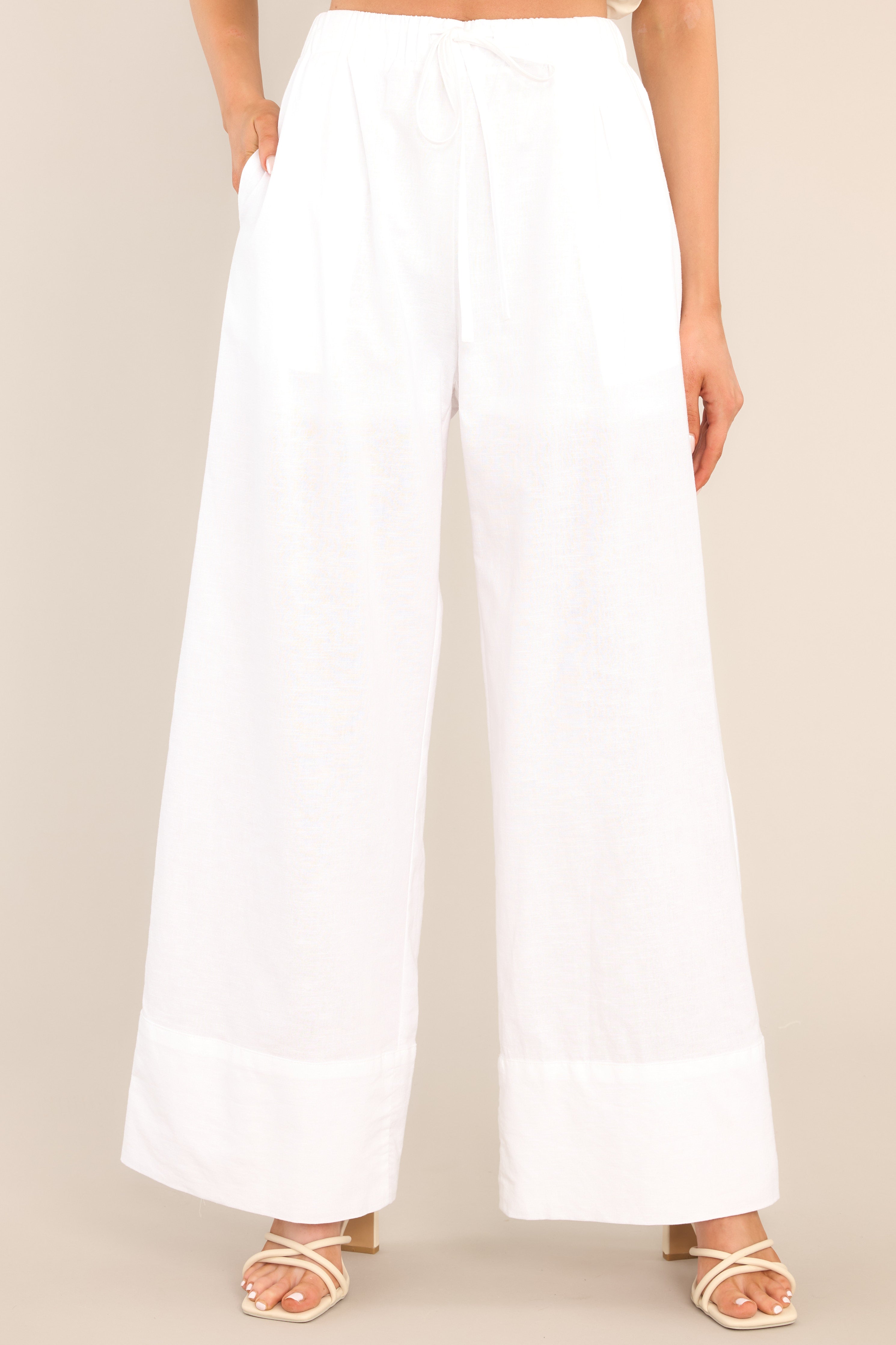 These white pants feature a high waisted design, an elastic waistband with a self-tie feature, functional pockets, and a thick ankle cuff. 