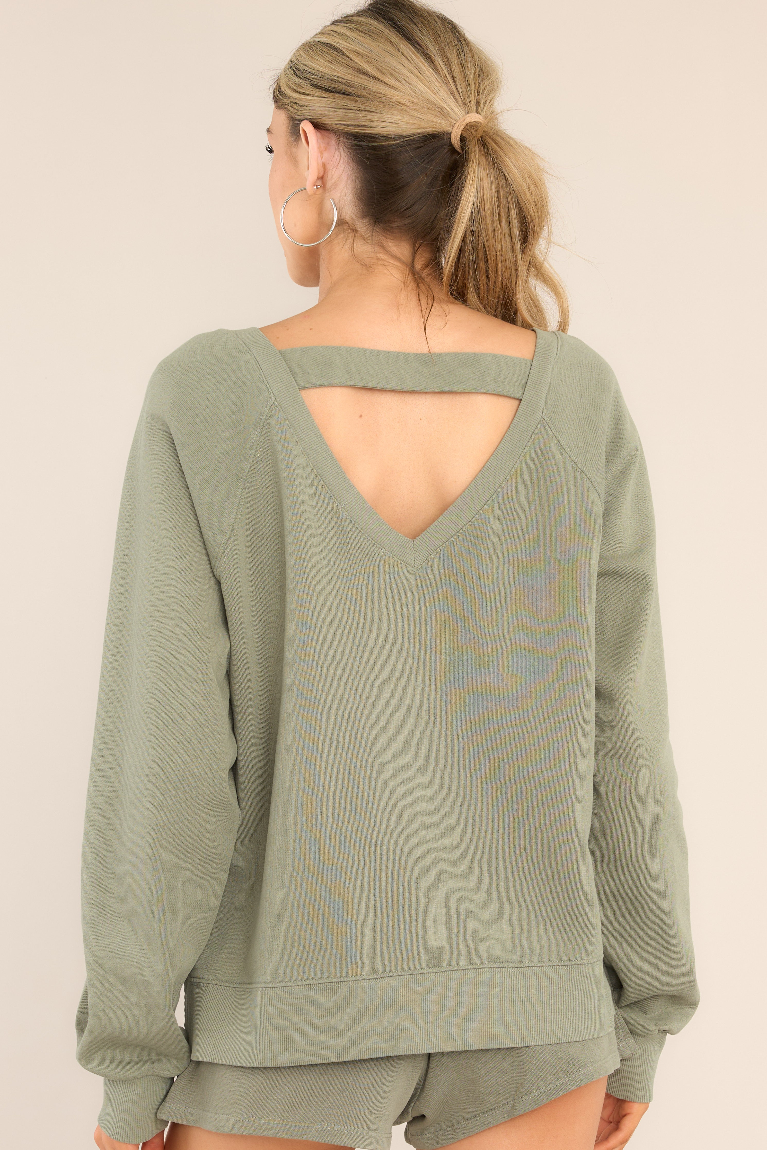 Back view of this sweatshirt that features a ribbed wide v-neckline, an intentional front-seam detail, fitted ribbed sleeve cuffs, a small split hem on the sides, and an open v-shaped back detail.