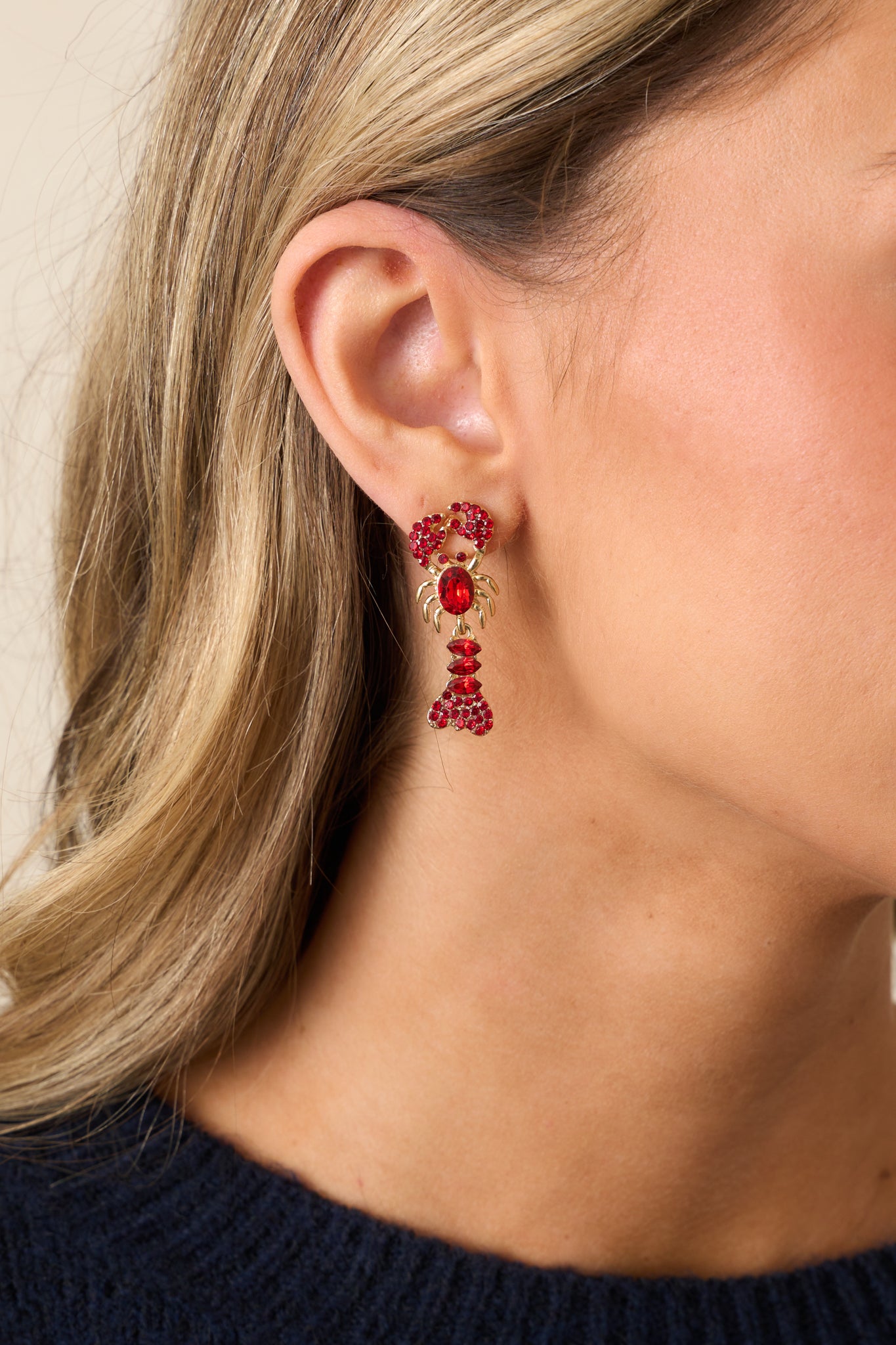 A close-up of the red rhinestone earrings, showcasing the gold hardware, lobster design, and the shimmering red rhinestones covering the tail and bodice.