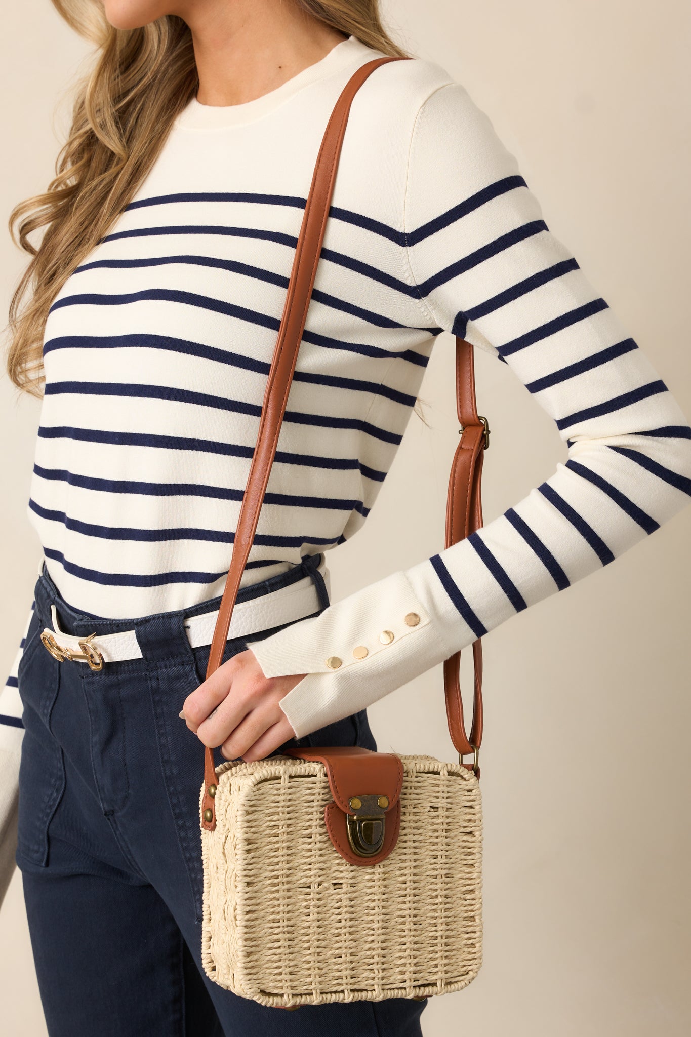 A handbag with a square shape, showcasing the white wicker material, bronze tuck lock closure, and brown faux leather shoulder strap.