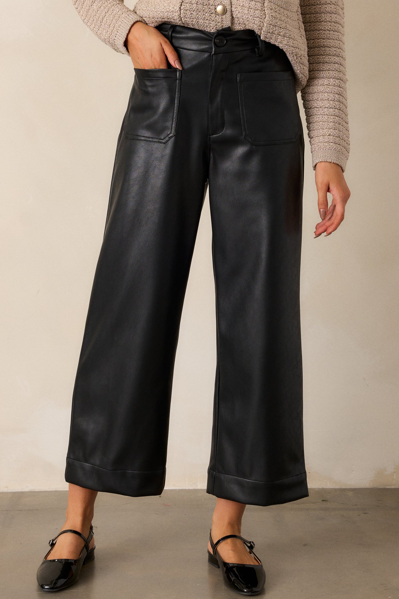 Cropped view of the black pants, emphasizing the wide-leg cut, smooth faux leather texture, and visible belt loops at the waist.