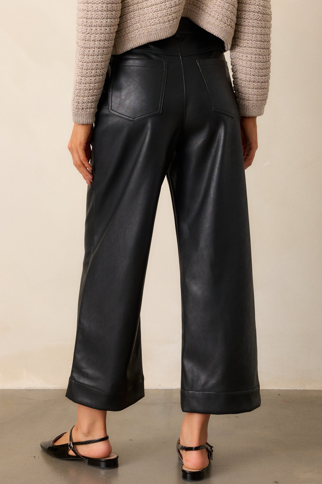 Back view of the pants, showcasing the functional back pockets, belt loops, and smooth faux leather finish across the wide-leg design.