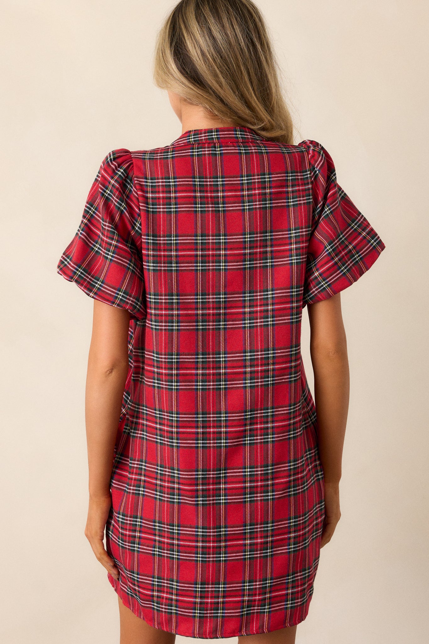 Back view of a red mini dress featuring a v-neckline, plaid design, black sequin bow detailing, and puff sleeves with elastic cuffs.