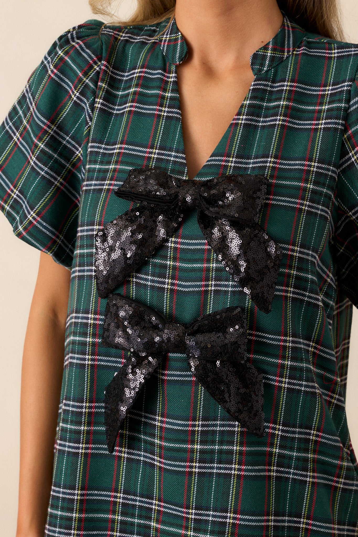 Close up of the black sequin bows on the v-neck of this green plaid mini dress.