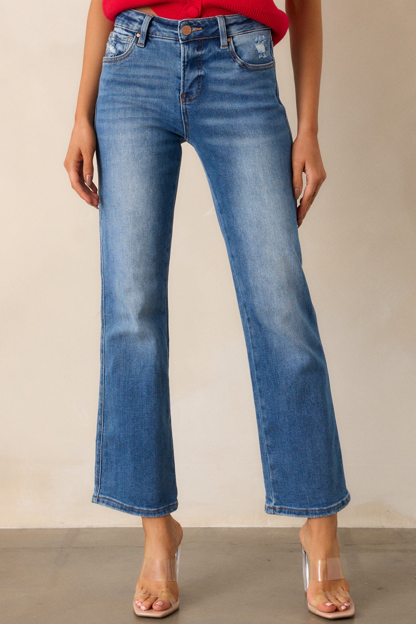 Front view of medium wash jeans featuring a high-rise design, functional front and back pockets, a button and zipper closure, a slightly distressed finish, and a straight leg cut.