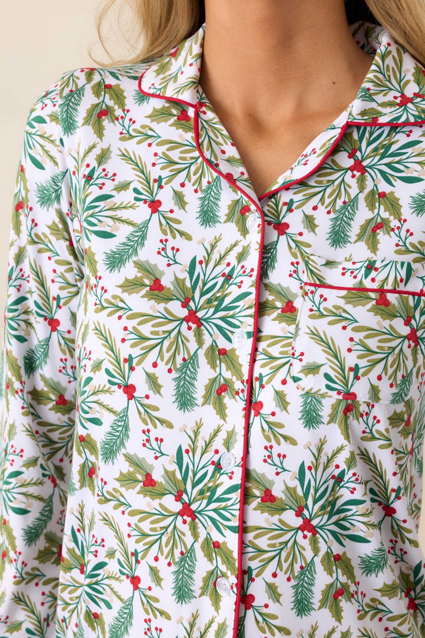 Close-up of mistletoe print on ivory pajama top, showcasing red trim and smooth fabric texture.