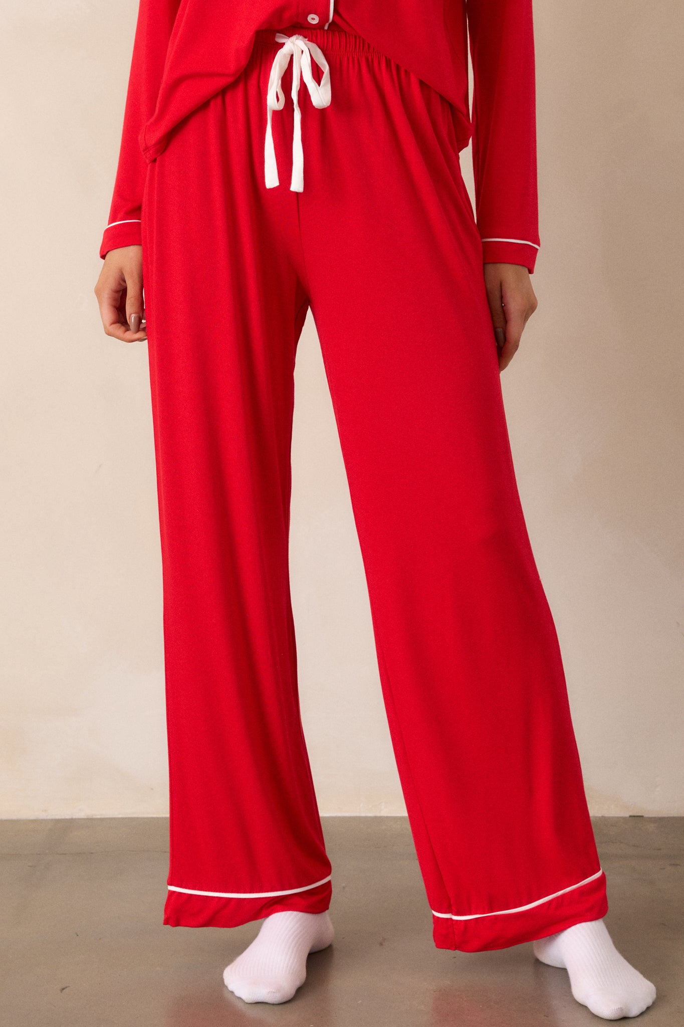 Front view of red Pajama Pants featuring an elastic drawstring waistband with a white string, white trim detailing and long relaxed pant legs.