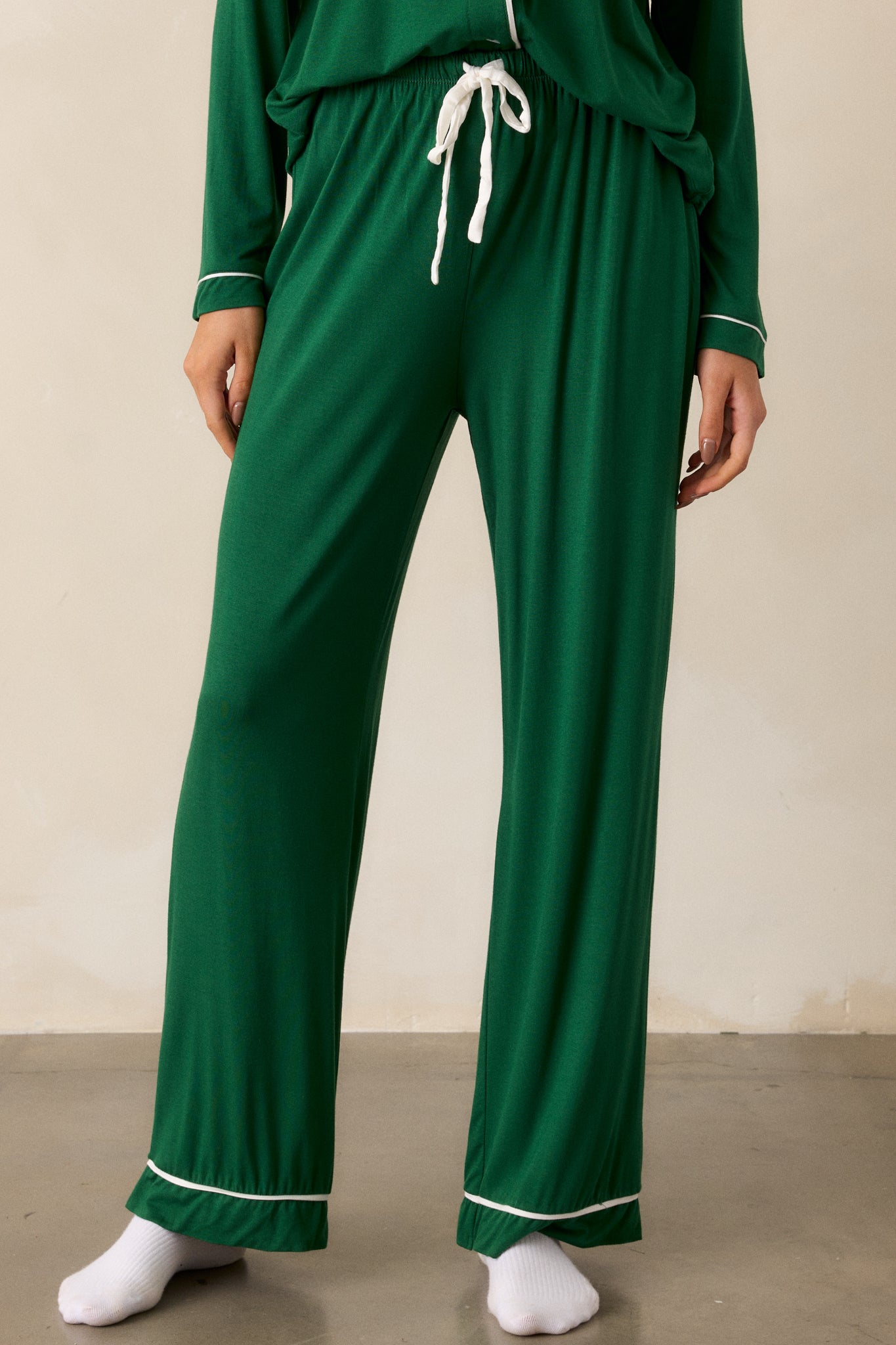 Close up view of forest green Pajama Pants featuring an elastic drawstring waistband with a white string, white trim detailing and long relaxed pant legs.