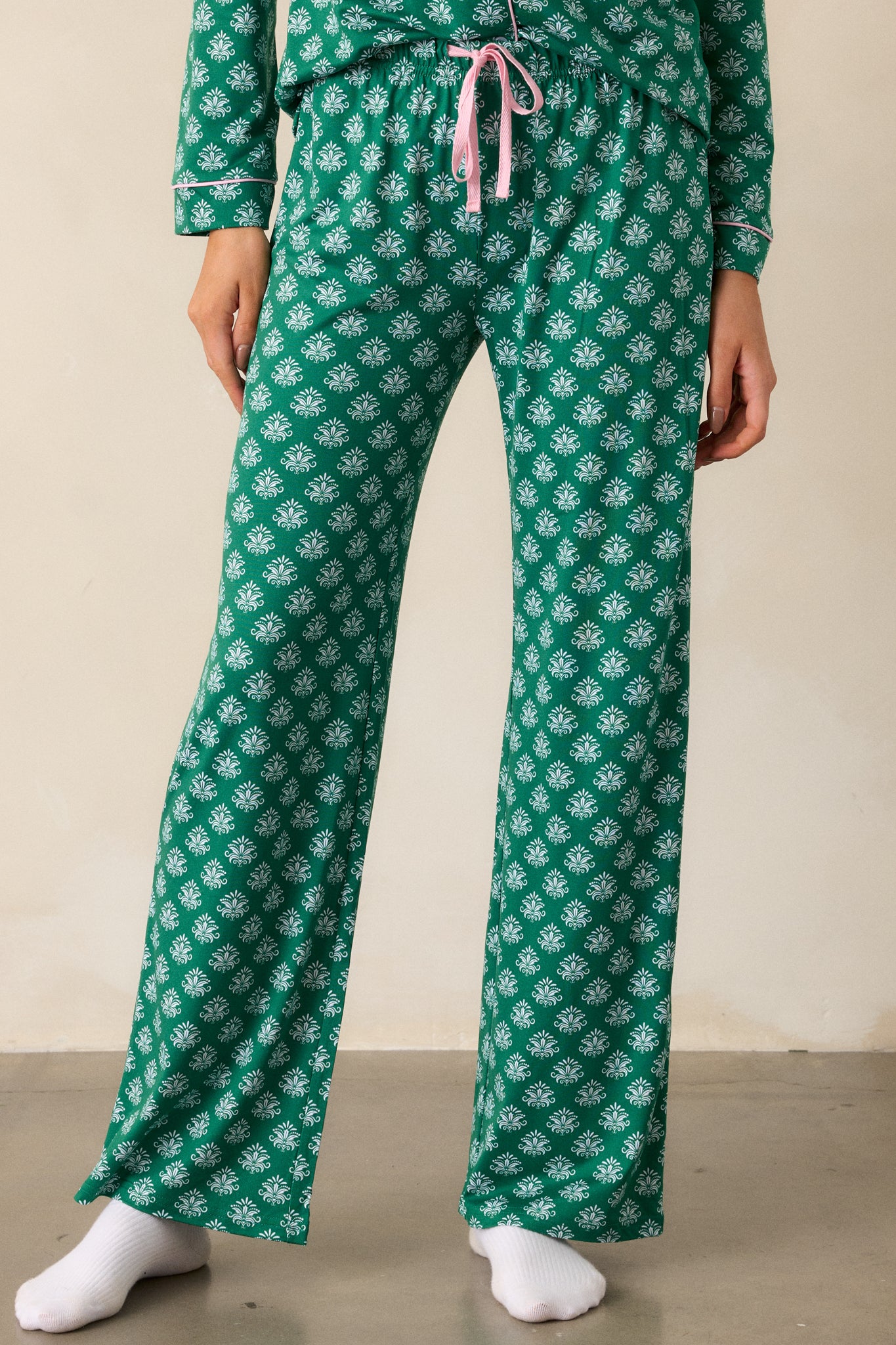 A detailed view of the lower portion of the pants, highlighting the relaxed fit and the consistent Fleur de Lis design along the green fabric.